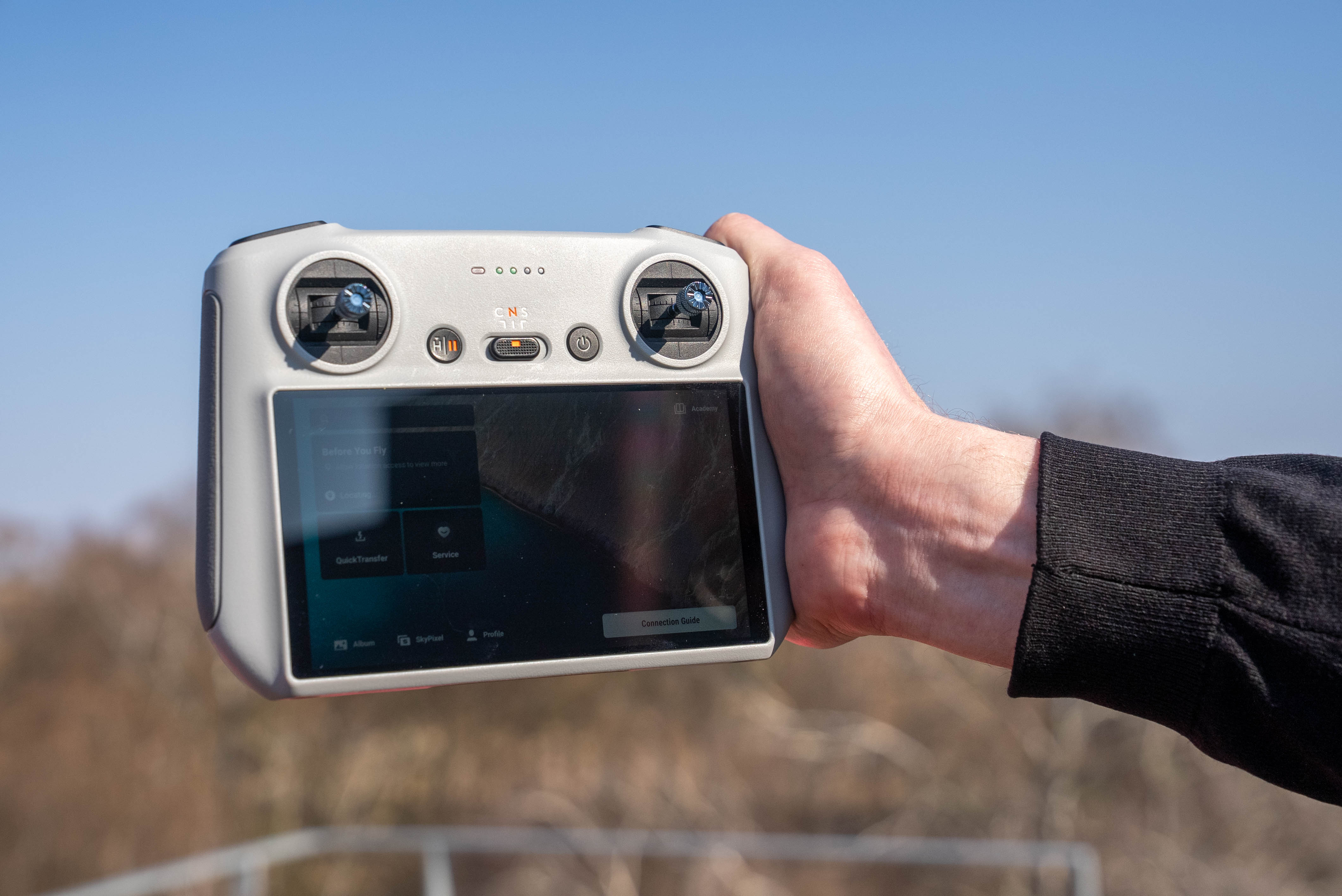 Hand, die die Drohnenfernsteuerung DJI RC hält. Im Hintergrund Bäume und blauer Himmel. Aufgenommen von Joel Arias mit einer Sony FX3.
