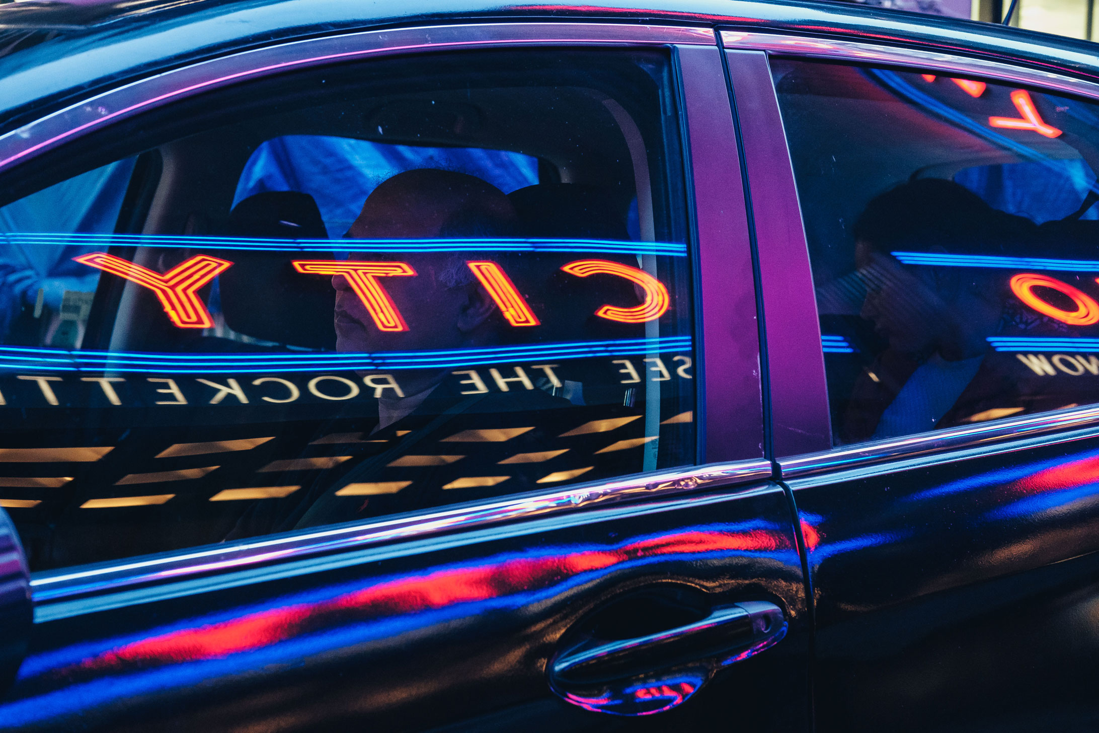 Person driving through Manhattan with a reflection of Radio City Music Hall on car window, photo by Manuel Pena.