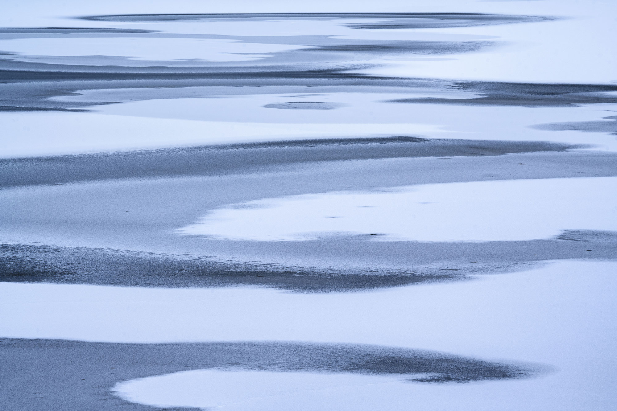Icy water surface with individual snow patches, creating a pattern, shot by Kilian Schönberger