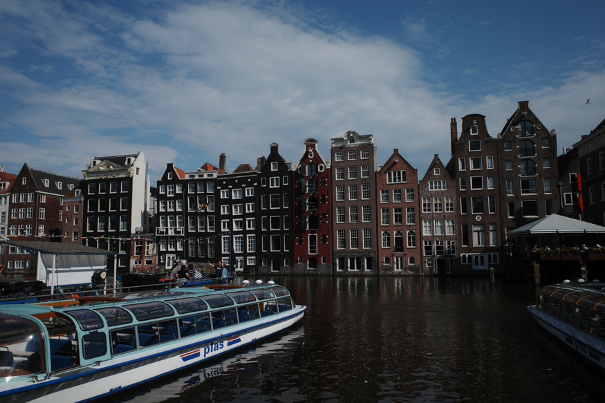 A classic view of the dancing houses at Amsterdam’s Damrak, captured with tour boats in the foreground and reflections on the water, shot by Hermann Furin