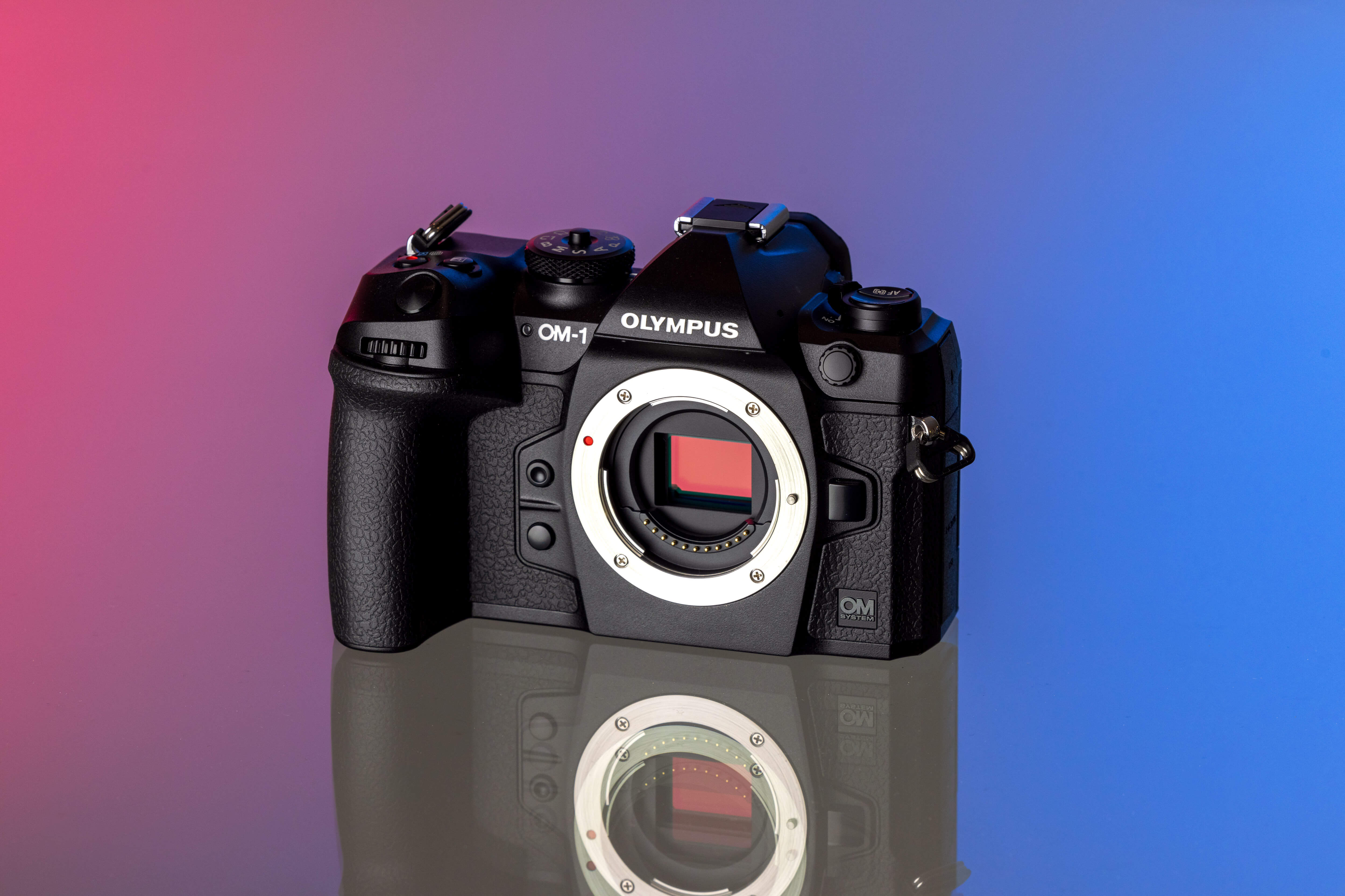 Een systeemcamera ‘Olympus OM-1-2’ wordt tentoongesteld tegen een achtergrond met een kleurverloop van roze naar blauw.