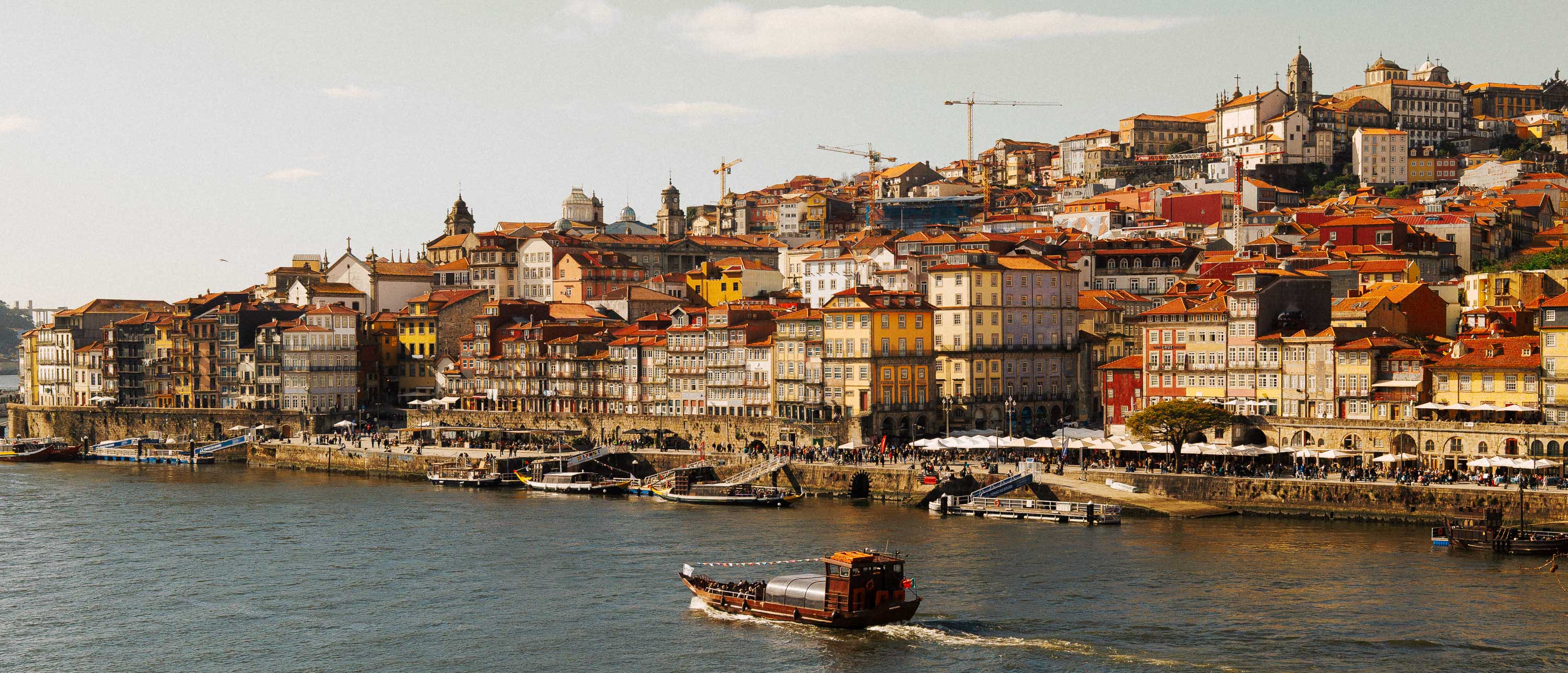Panoramaaufnahme des nördlichen Porto im Format 21:9, auf der ein traditionelles Rabello-Boot flussabwärts fährt. Aufgenommen von Connor Redmond mit der Sigma BF von der Südseite der Stadt.
