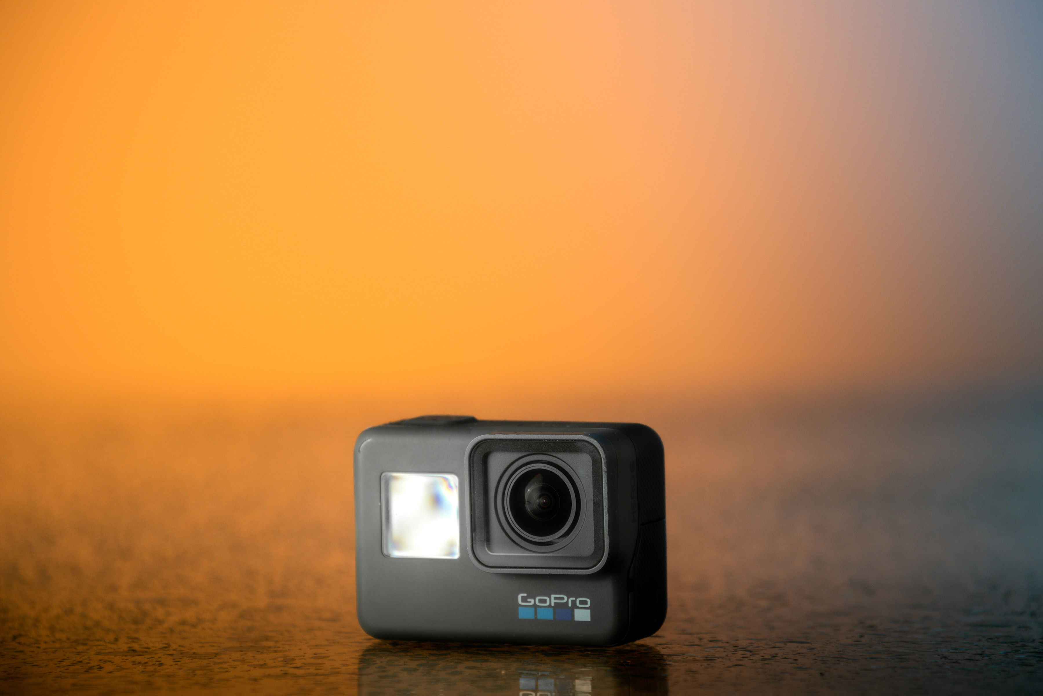 Image of a GoPro Hero 6 with an orange sunset background on a wet table.