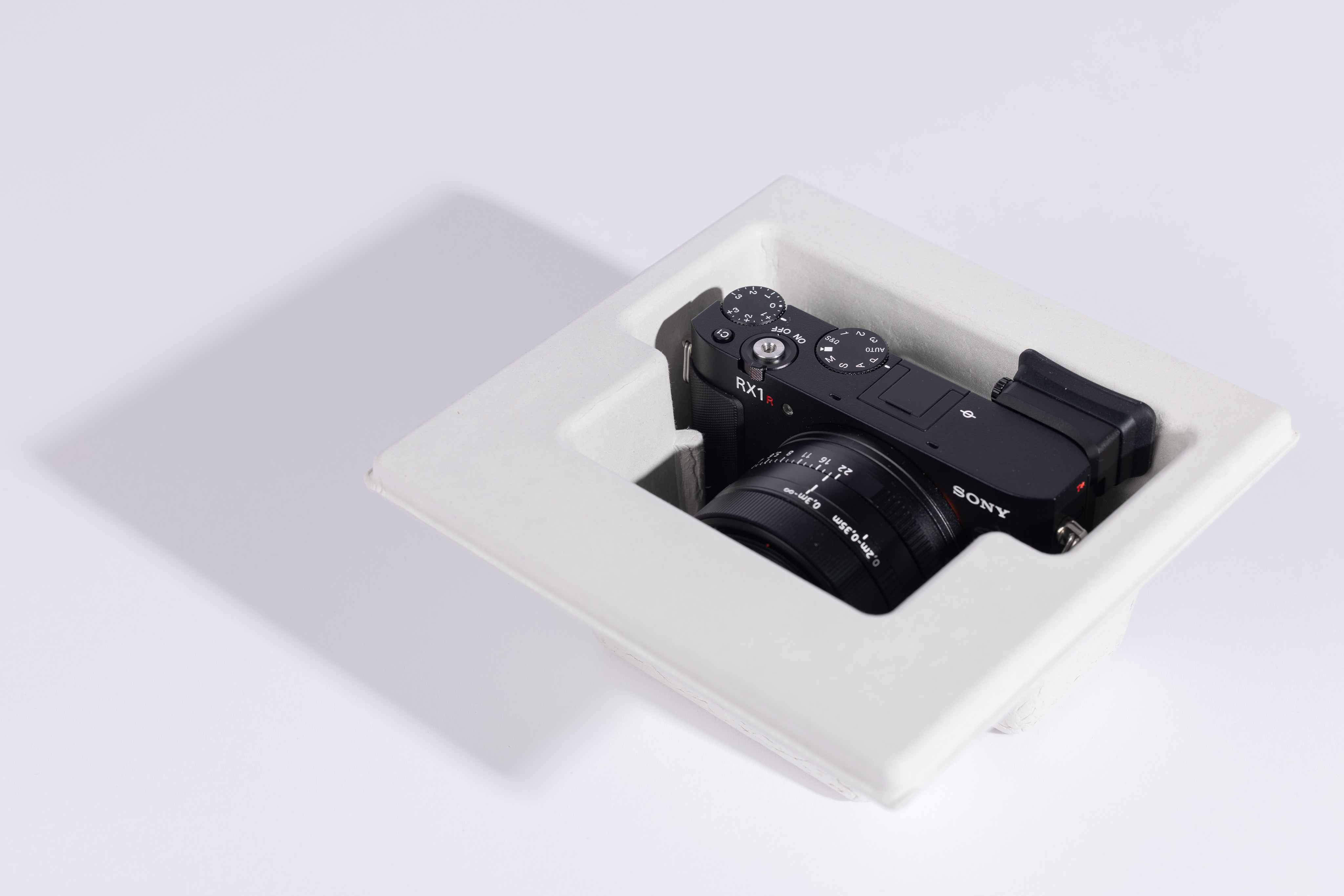 Die Kompaktkamera Sony RX1R III von oben, in schützender weißer Verpackung mit sichtbarem festem 35-mm-Objektiv und oberen Einstellrädern.