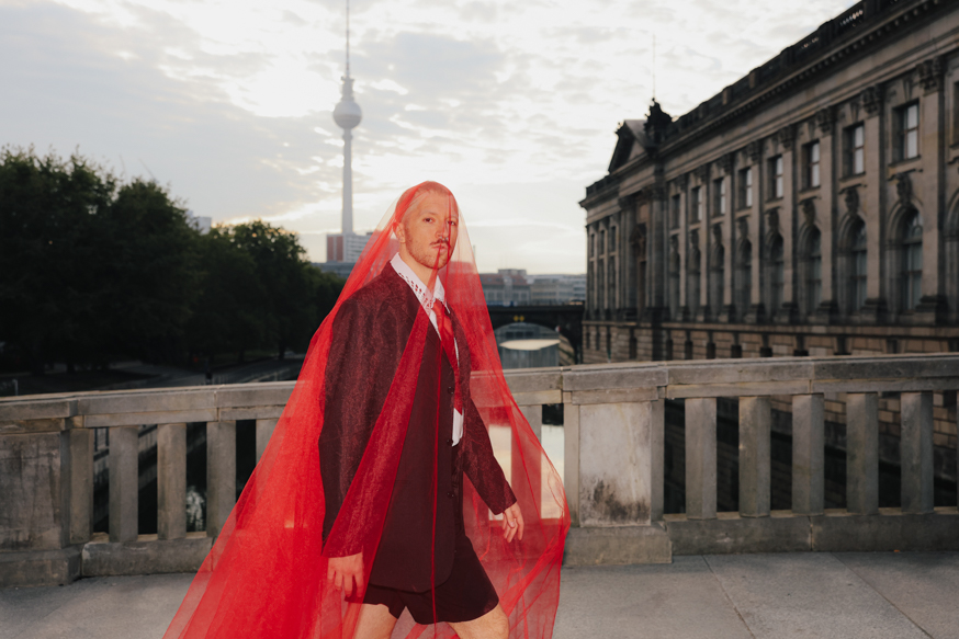 A striking wedding portrait with the groom covered in a red veil and Berlin’s iconic TV Tower in the background.