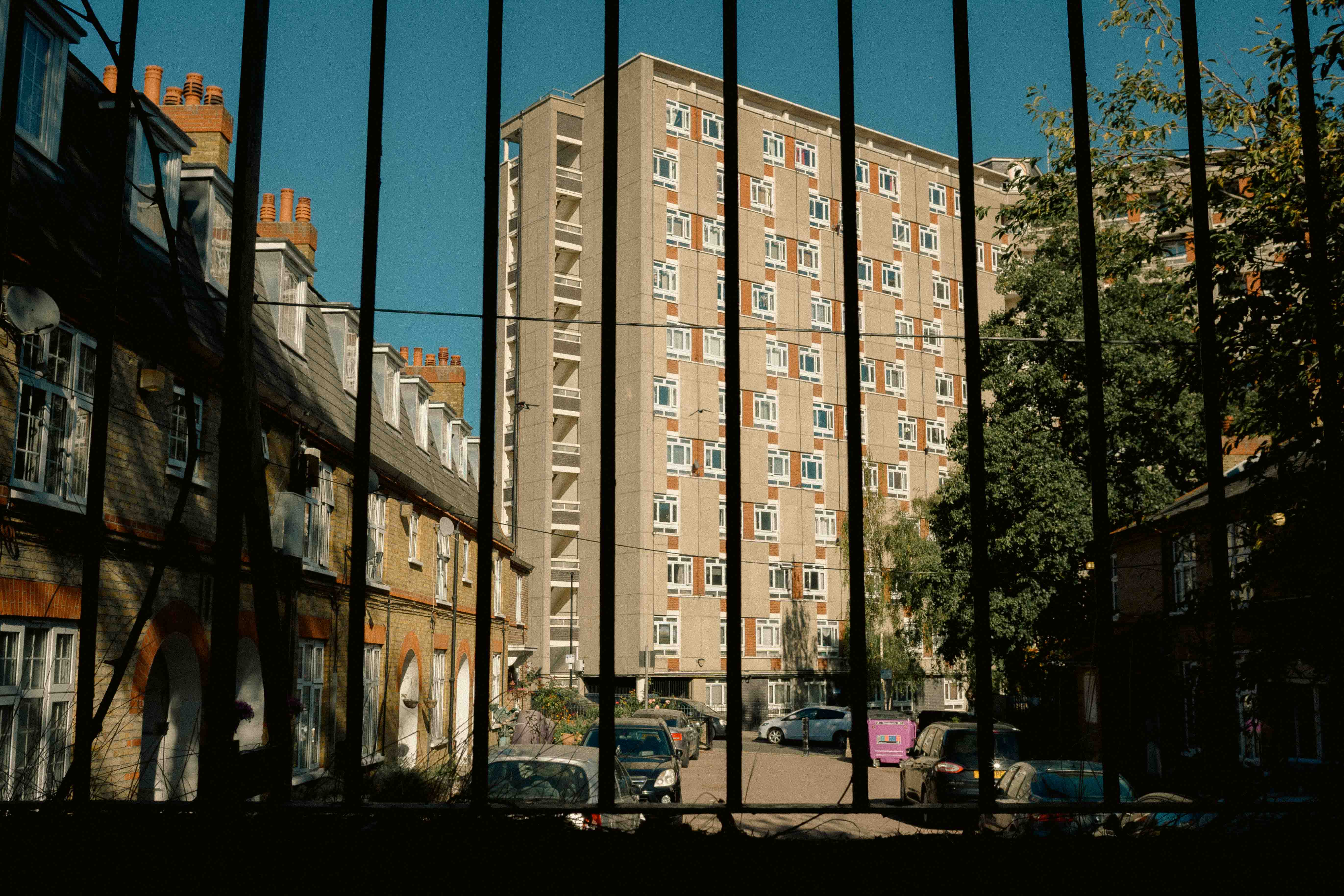 A block of flats in London, obscured by black railings in the foreground. By Connor Redmond.