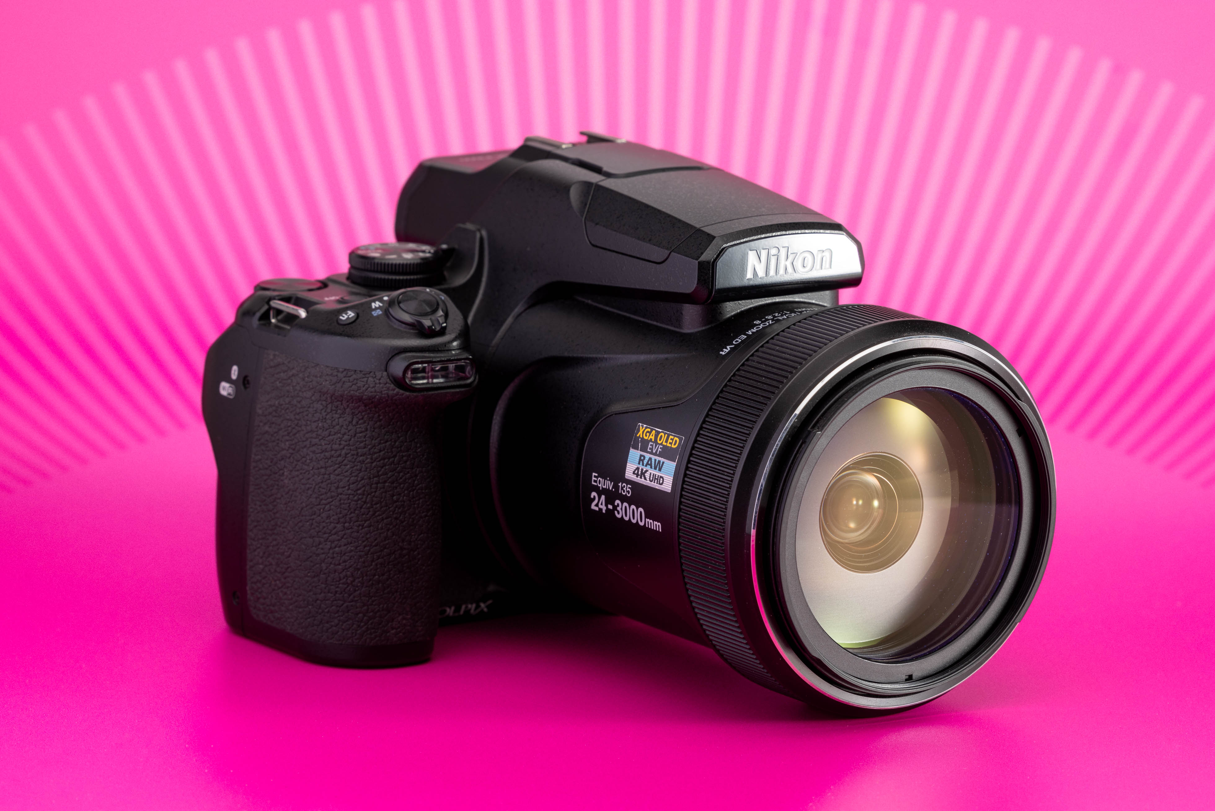 Nikon Coolpix P1000 fotografiada sobre fondo rosa, con objetivo zoom integrado. Foto de Connor Redmond