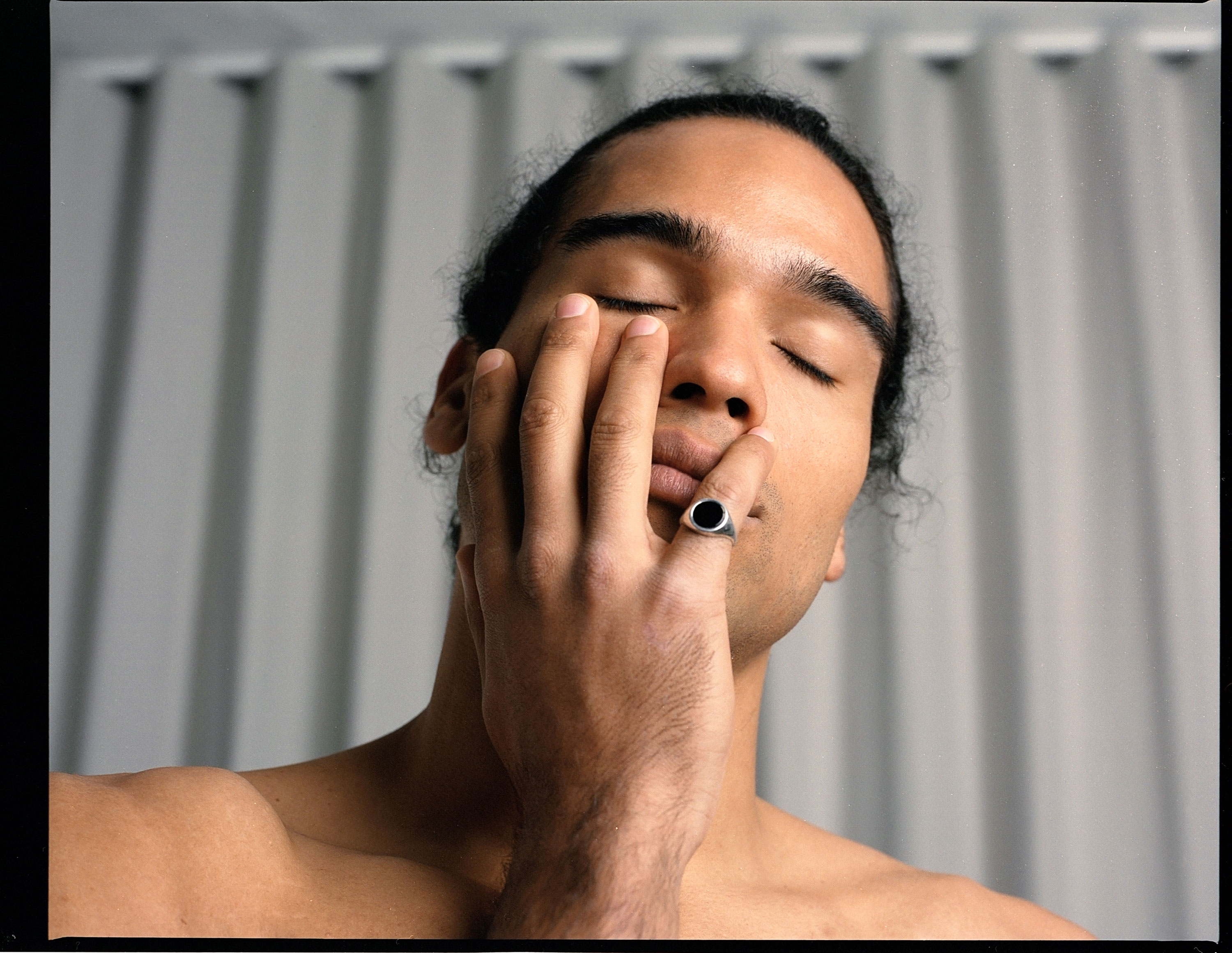 Portrait of a Person of Colour with closed eyes and black ring on their little finger, putting their right hand on their face, shot by Samia Rachel.