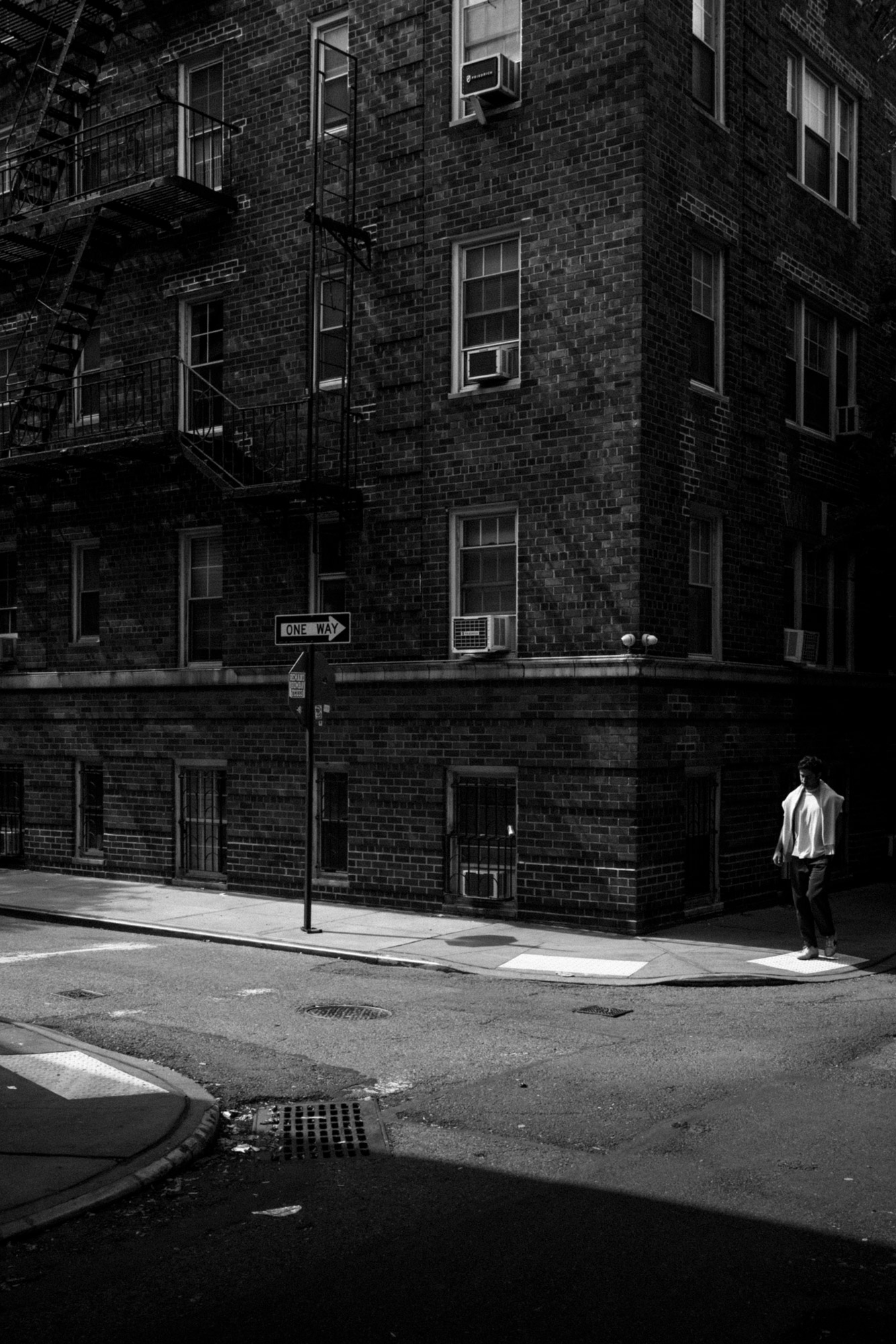 A black-and-white photo of a person standing on a street corner by a building