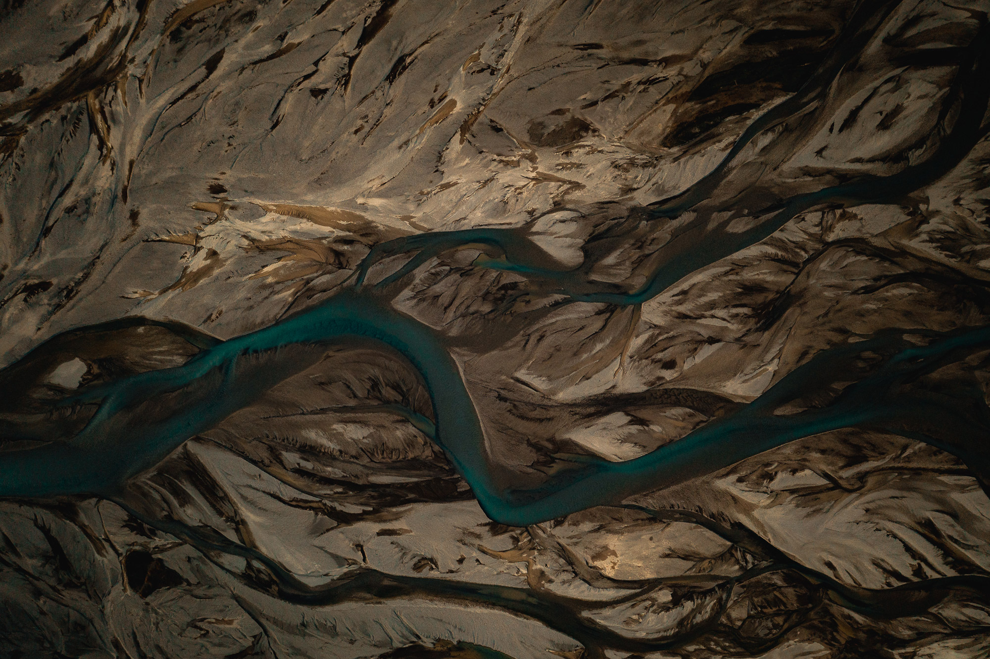 Eine Drohnenaufnahme von einem blauen Fluss, der durch ein dunkelbraunes Tal in Island fließt, aufgenommen von Paul Watson mit einer DJI Mavic 2 Pro