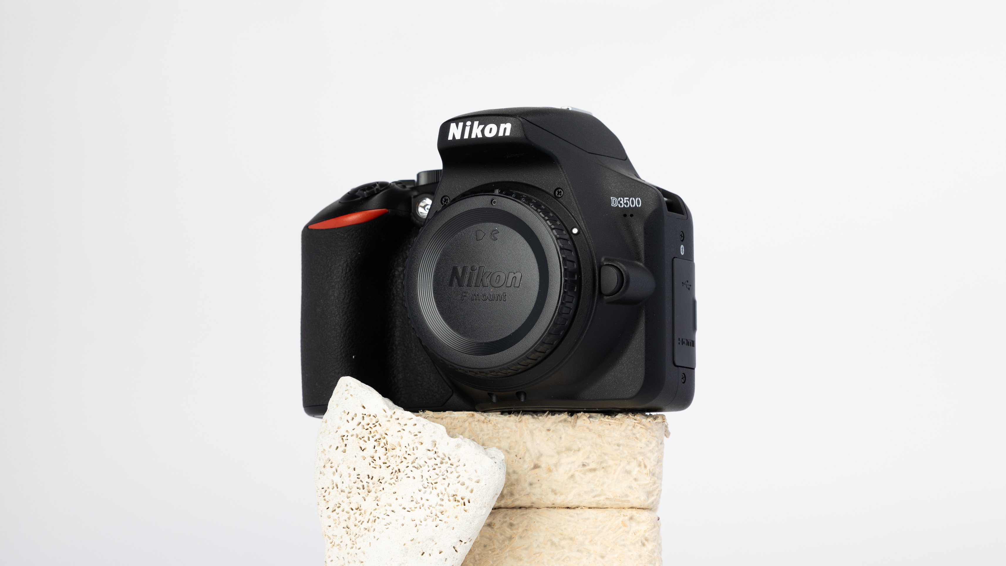 A product shot of a secondhand Nikon D3500 camera propped up on a rocky podium