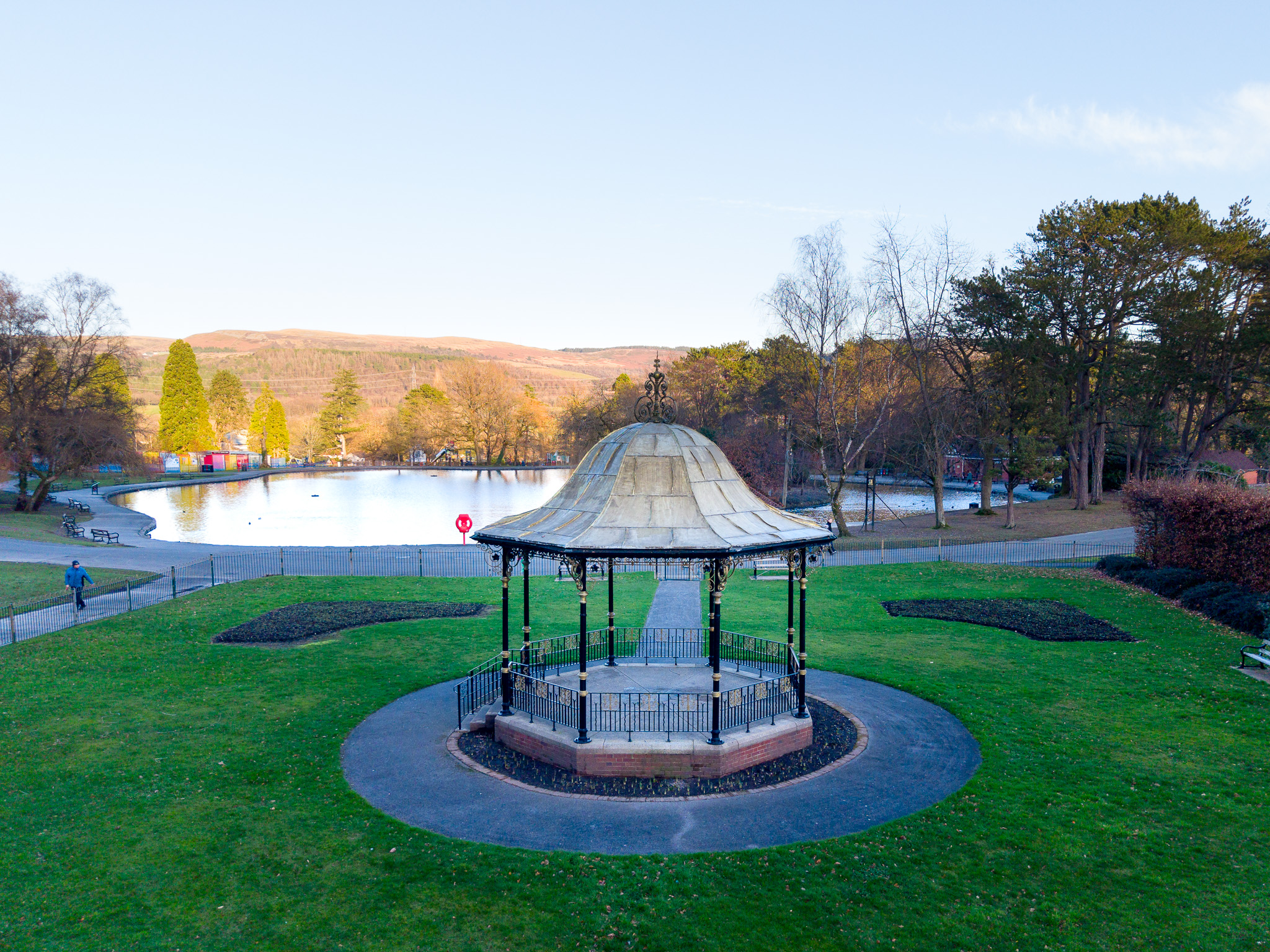 Imagem captada com o DJI Mini 5 Pro, mostrando um coreto num parque verde junto ao lago. A composição destaca a simetria do espaço, os caminhos circulares e a paisagem aberta em redor.