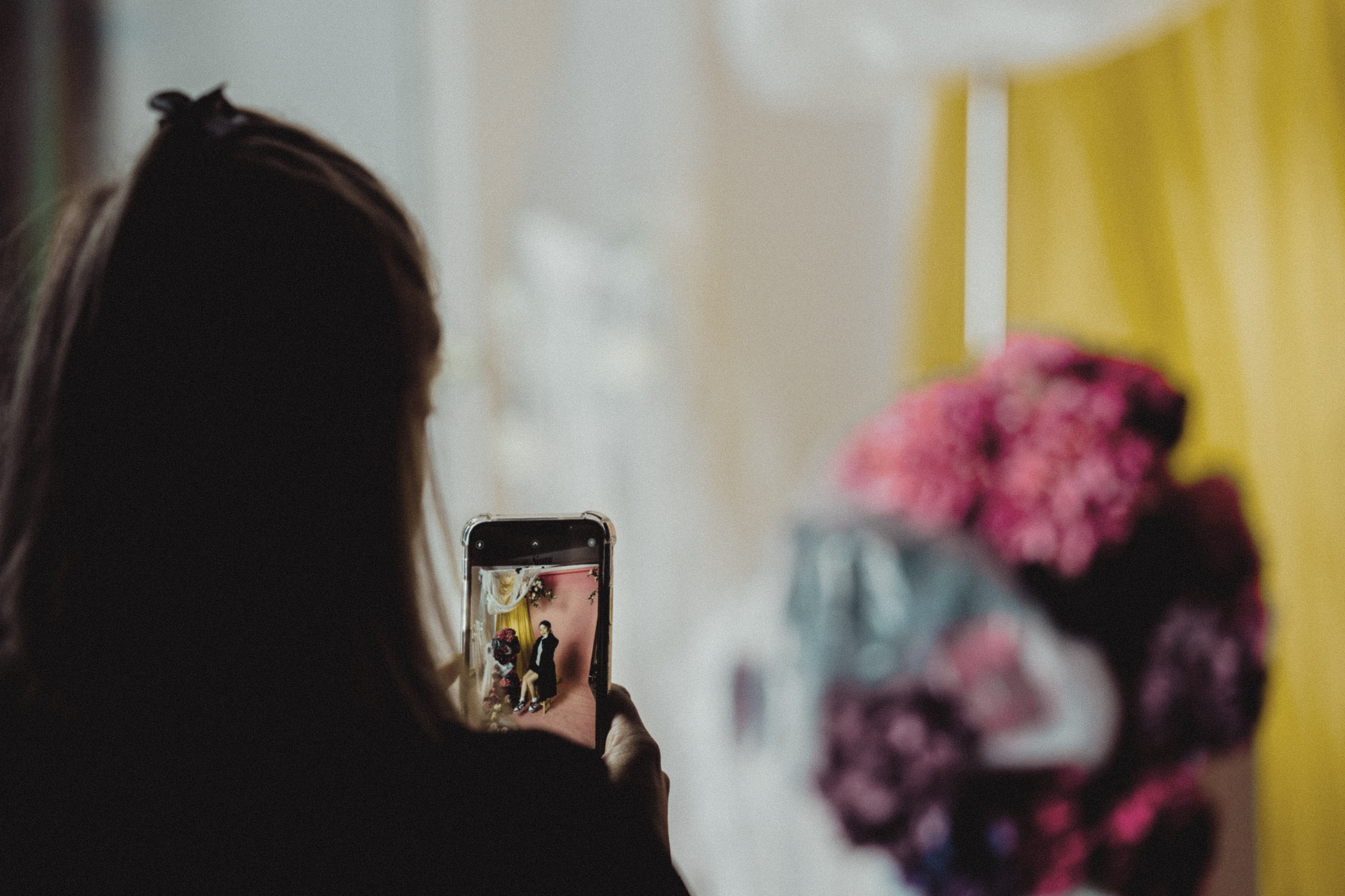 Eine Person mit langen Haaren fotografiert mit ihrem Smartphone einen großen Blumenstrauß