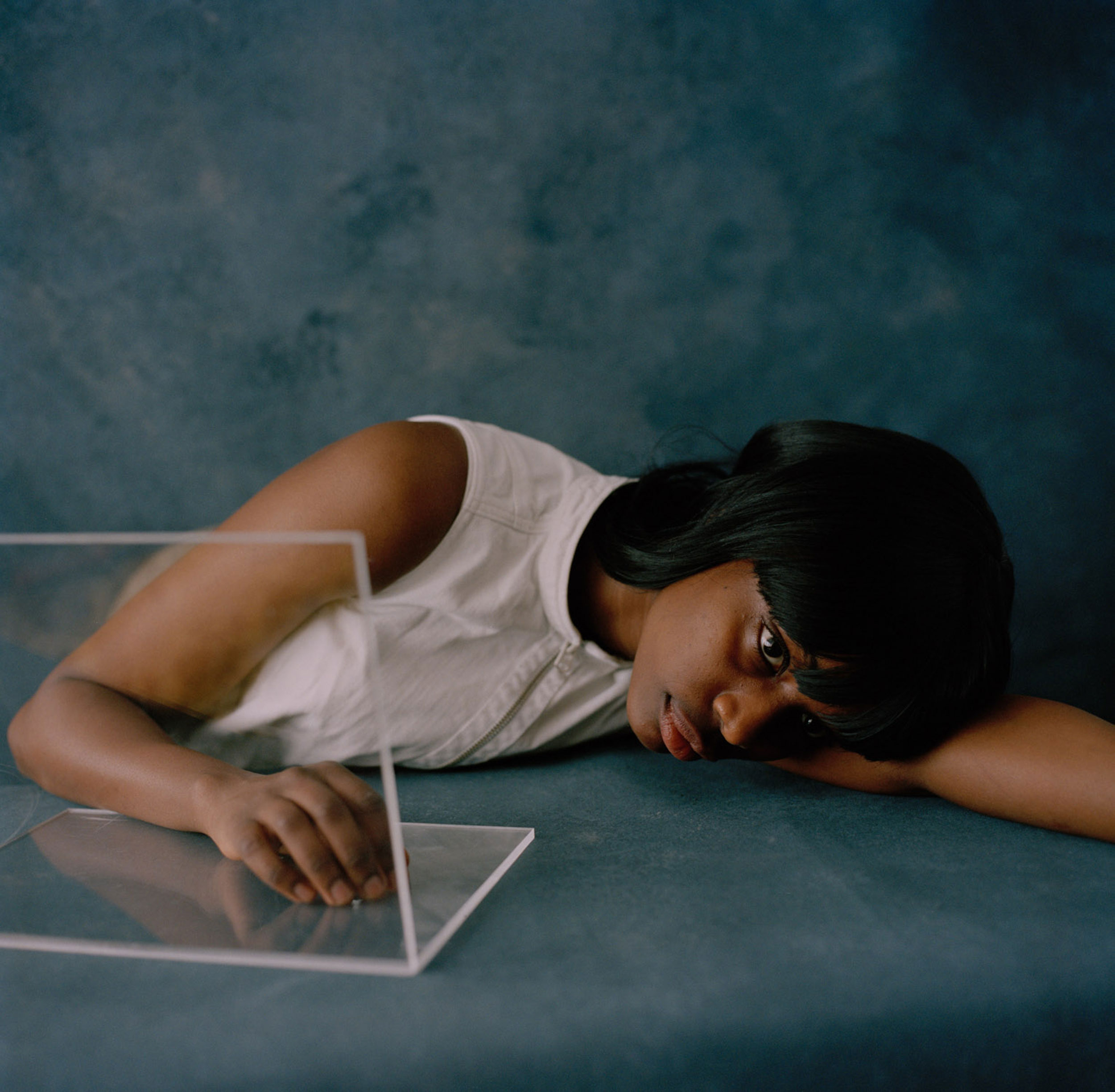 Black woman resting her head on her arm and looking into the void, against a blue background, shot by Nicole Benewaah 

