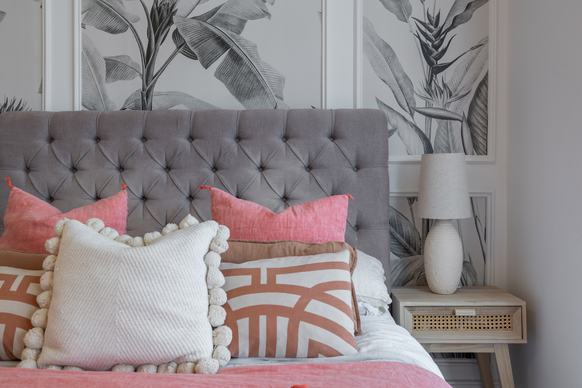 Roze en wit kussen op een bed met een grijze hoofdsteun en nachtkastje aan de zijkant, gefotografeerd door Paul Moore met de Canon EOS R6 Mark II.