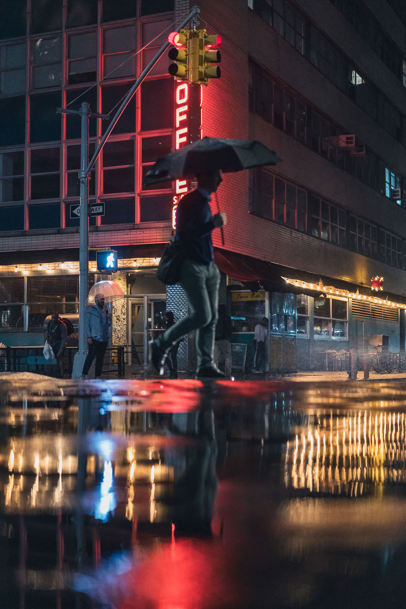 Persoon loopt met een paraplu op een regenachtige avond voor een rood neonbord op Union Square in New York City, foto door Manuel Pena op een Sony A7 III.