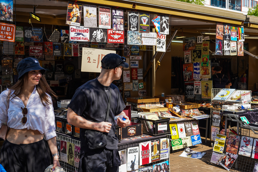 Een kleurrijke kraam met retro borden op de Amsterdamse Waterloopleinmarkt, vol grafische prints en levendige straatsfeer, gefotografeerd door Louise Kluit