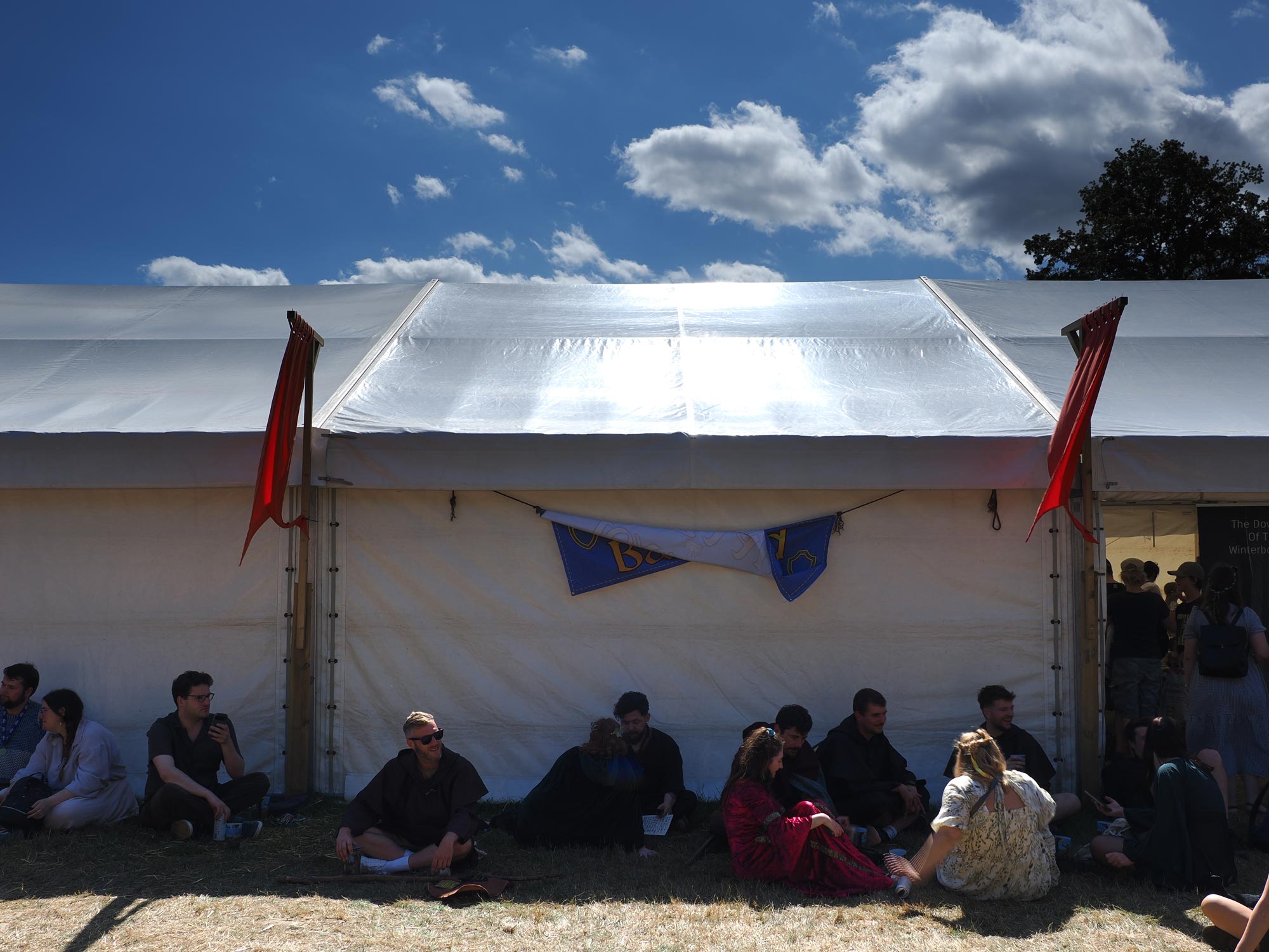 Menschen, die an einem sonnigen Tag auf einem Mittelalterfestival im Schatten eines Glockenzelts sitzen.