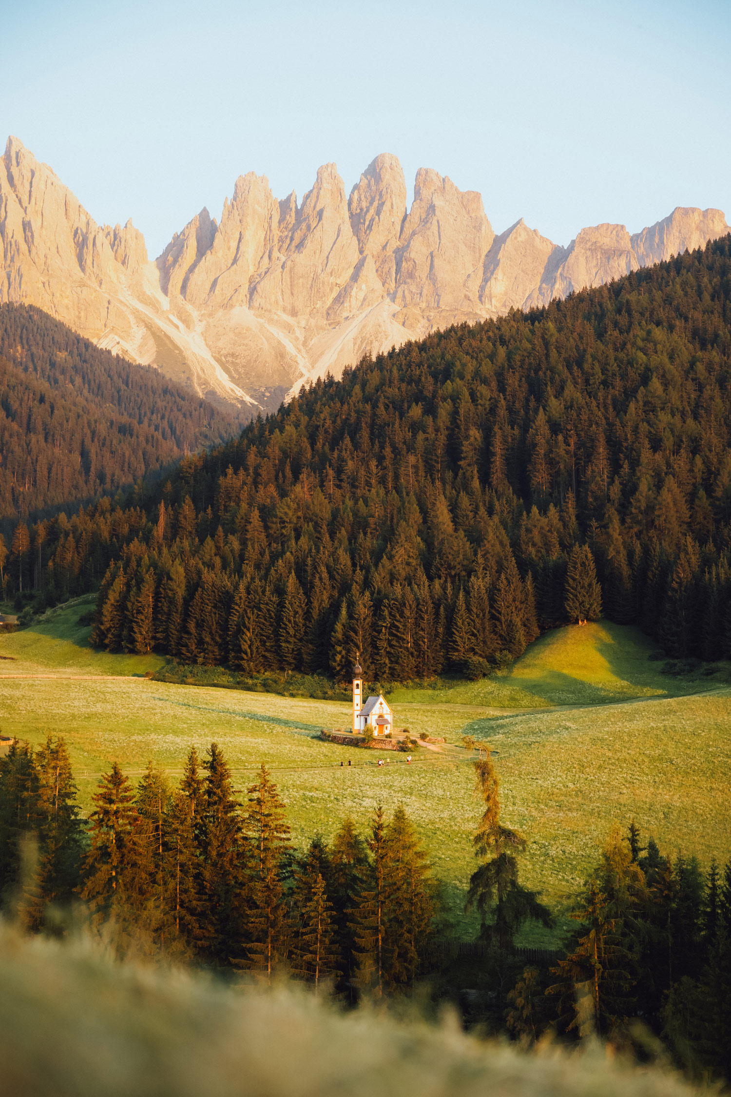 Eine weiße Kirche auf einem Feld mit Bäumen im Hintergrund und einer Bergkette in der Ferne, aufgenommen von Jacob Murray mit einer Canon R5 und RF 24-70 f2.8.