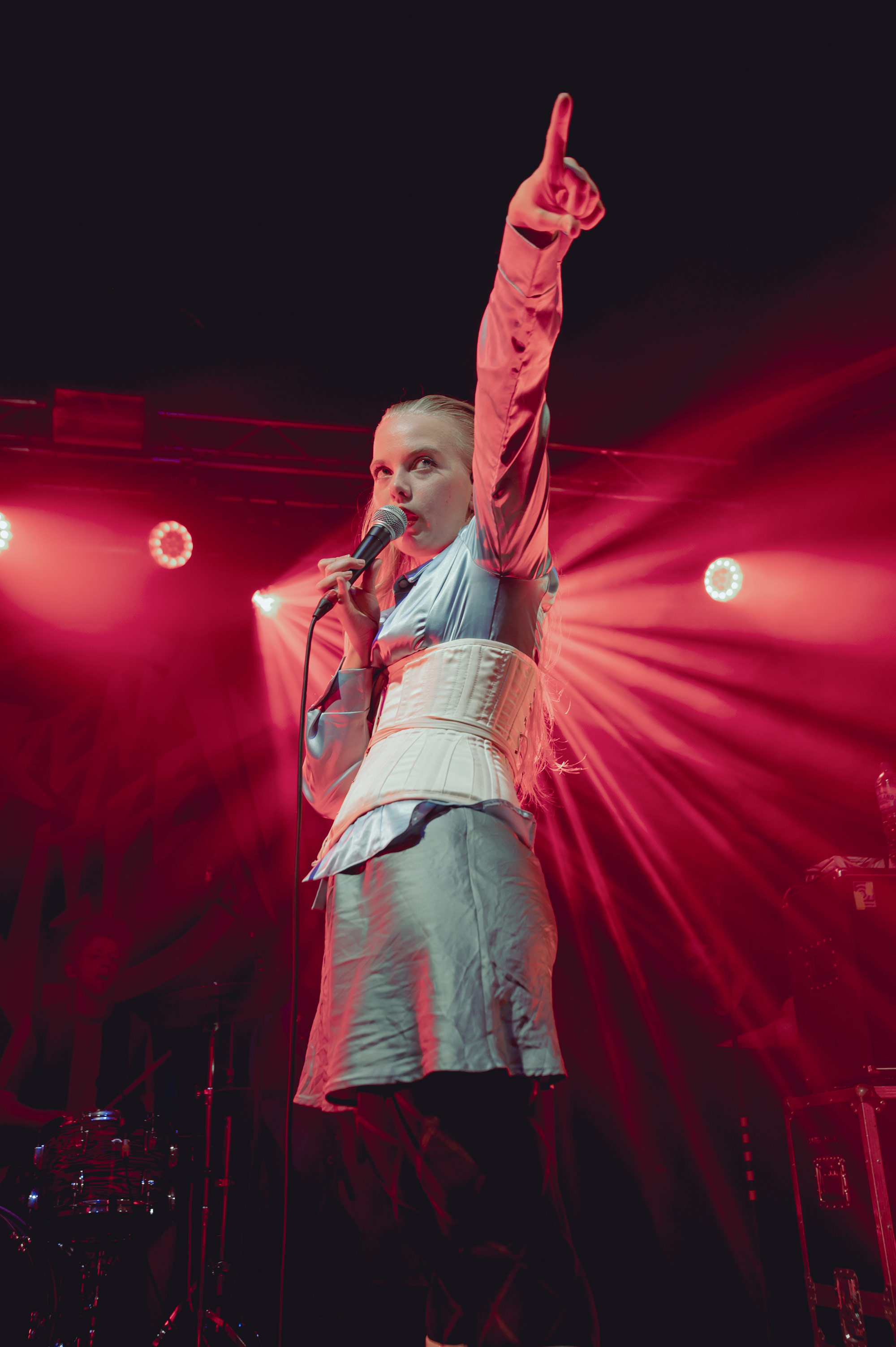 A photo of the lead singer of Dream Wife performing on stage pointing their finger in the air surrounded by pink lights, shot by Claudia Di Rito with a Nikon Z6
