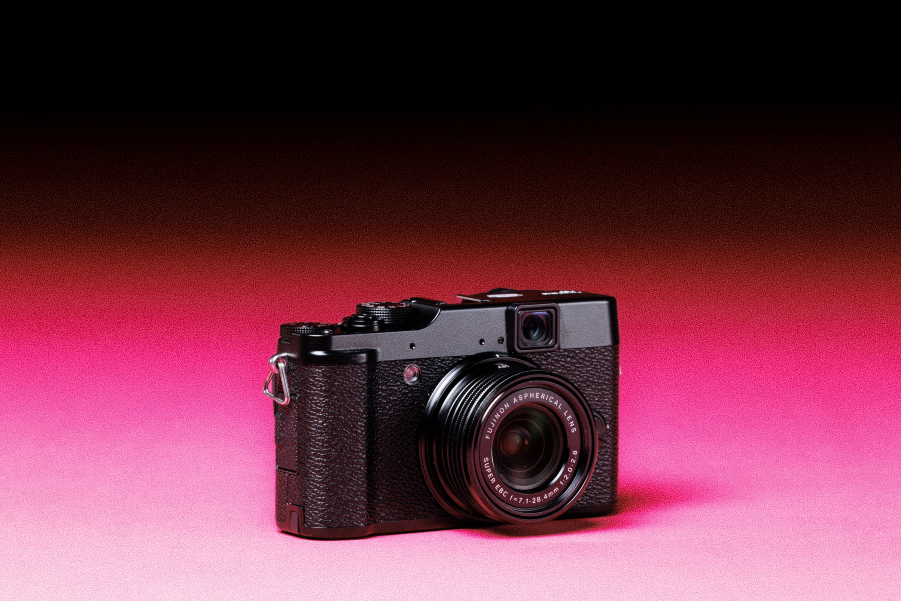 A used Fujifilm X10 with an added film-like grain effect on a graduated pink background. 