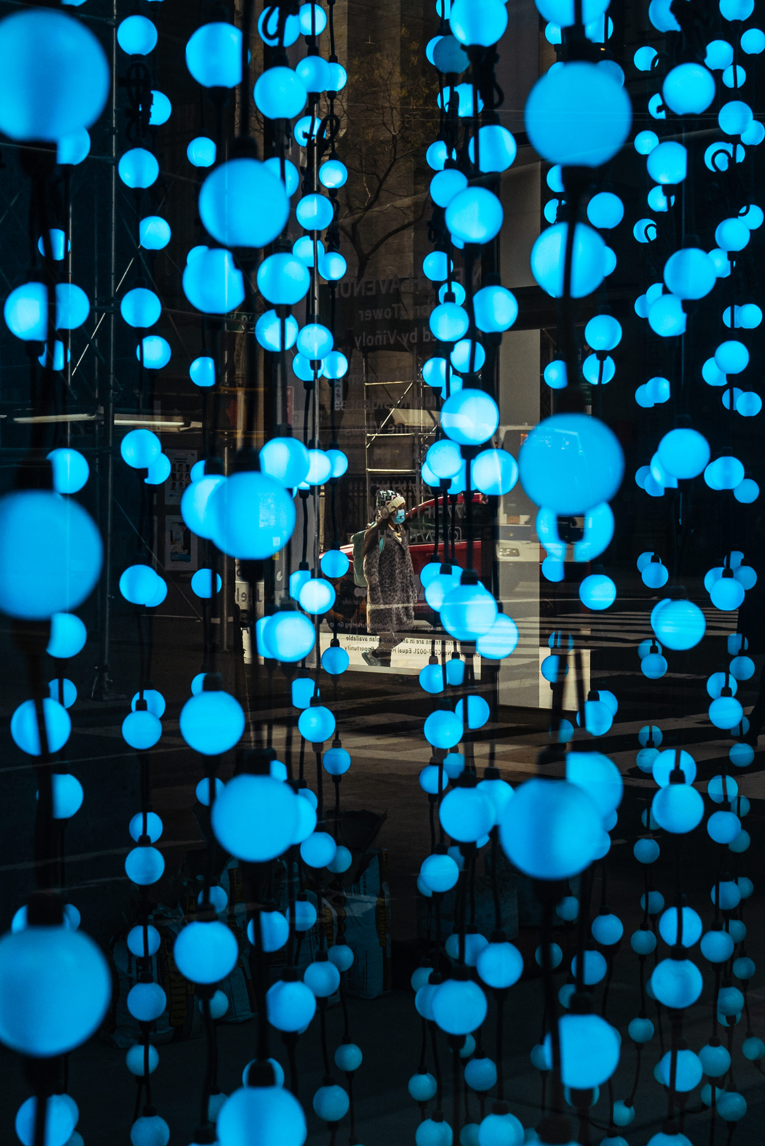 Blue light art piece with person walking outside in background in New York City, photo by Manuel Pena.