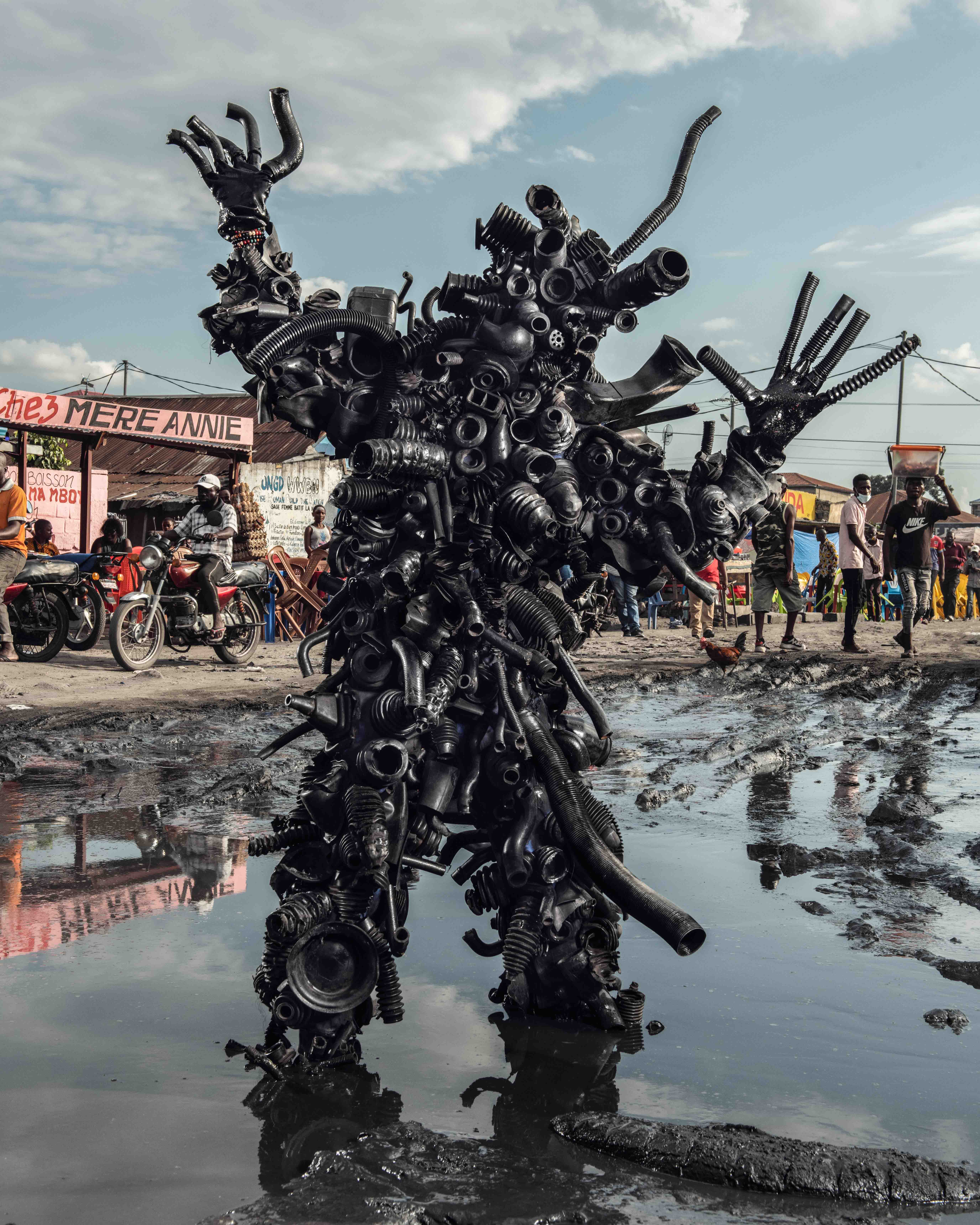 Eine riesige Gummifigur, die sich in Stephan Gladieus Homo Detritus aus dem Schlamm erhebt und das Chaos auf dem Markt in Kinshasa in rohe Umweltkunst verwandelt.
