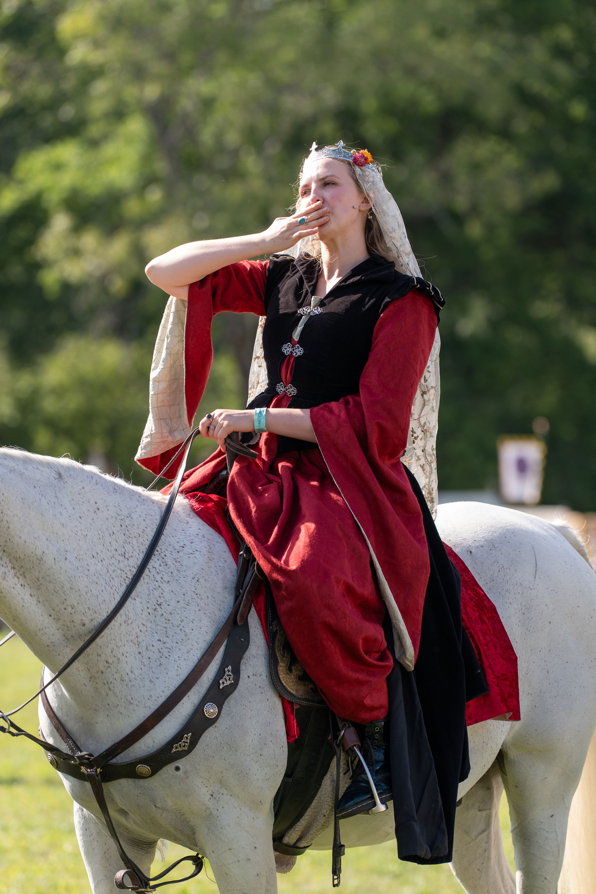 A person on the back of a white horse, dressed in a black and red costume and blowing a kiss to a crowd. The horse's head is out of frame.