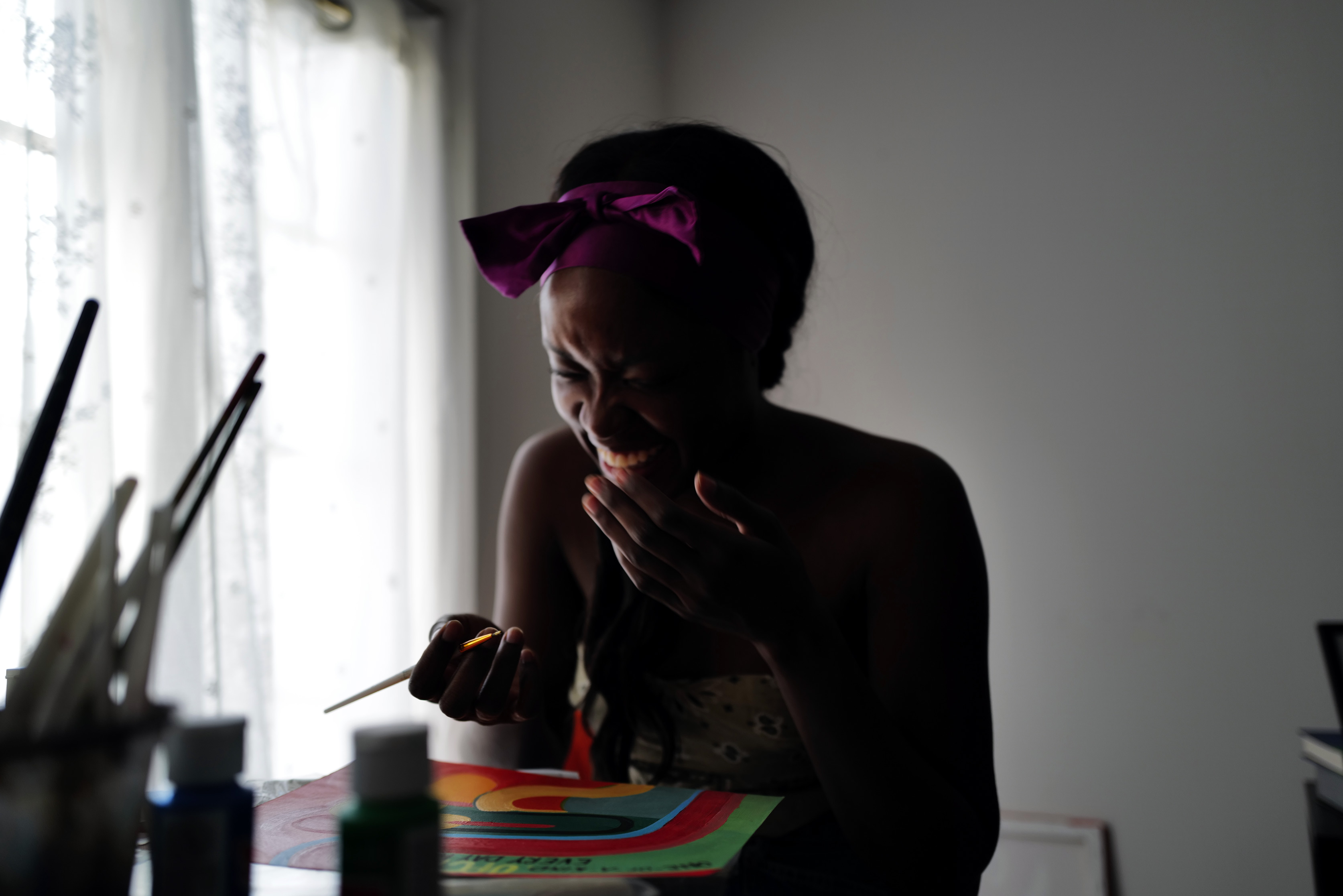 A person sitting at a table, holding a paint brush, laughing, shot by Drew Troutman