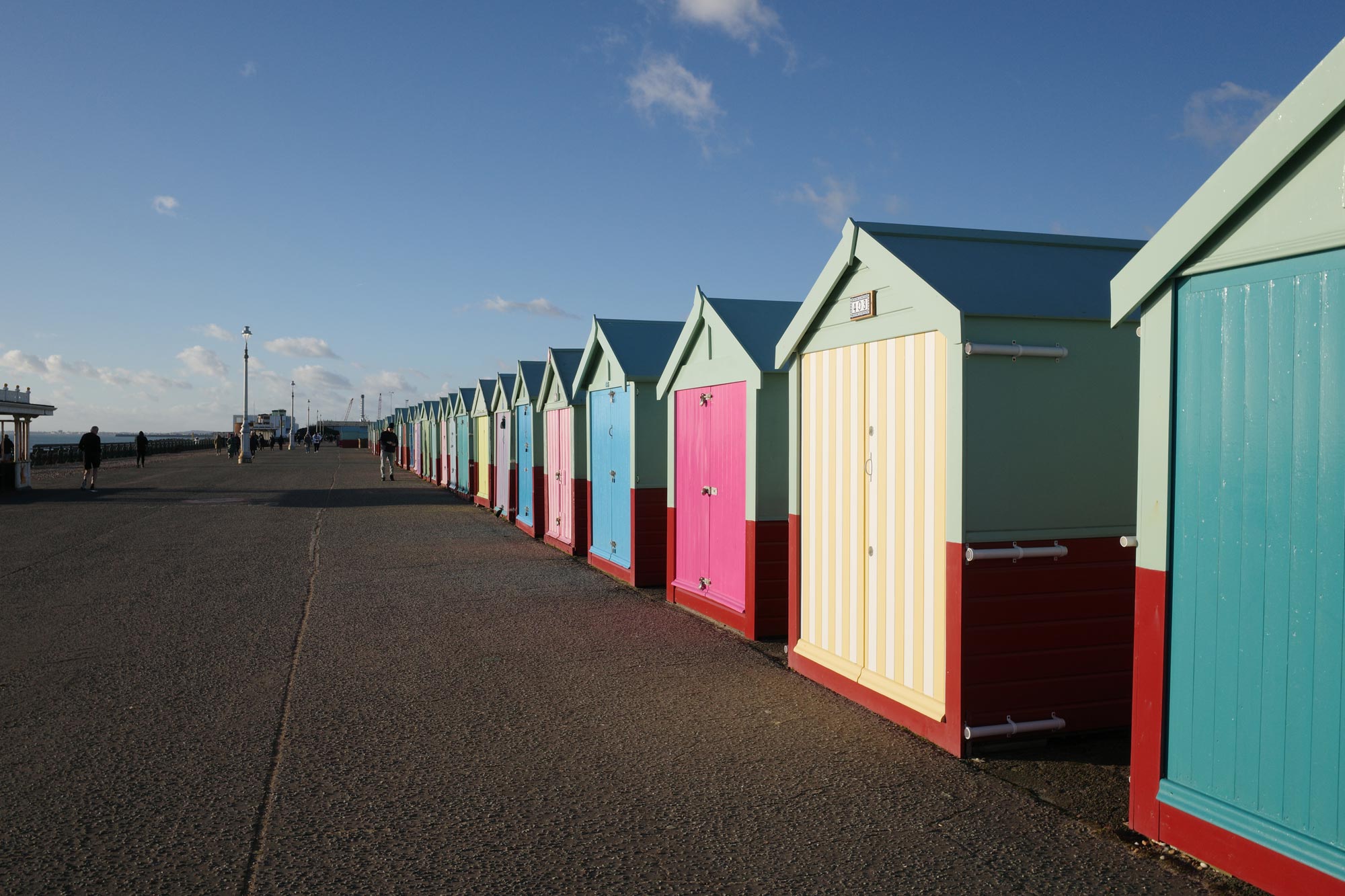 Een boulevard op een zonnige dag, vol met kleurrijke strandhuisjes. Boven je is een helderblauwe lucht met dunne witte wolken. Geen simulatiefilters toegevoegd.