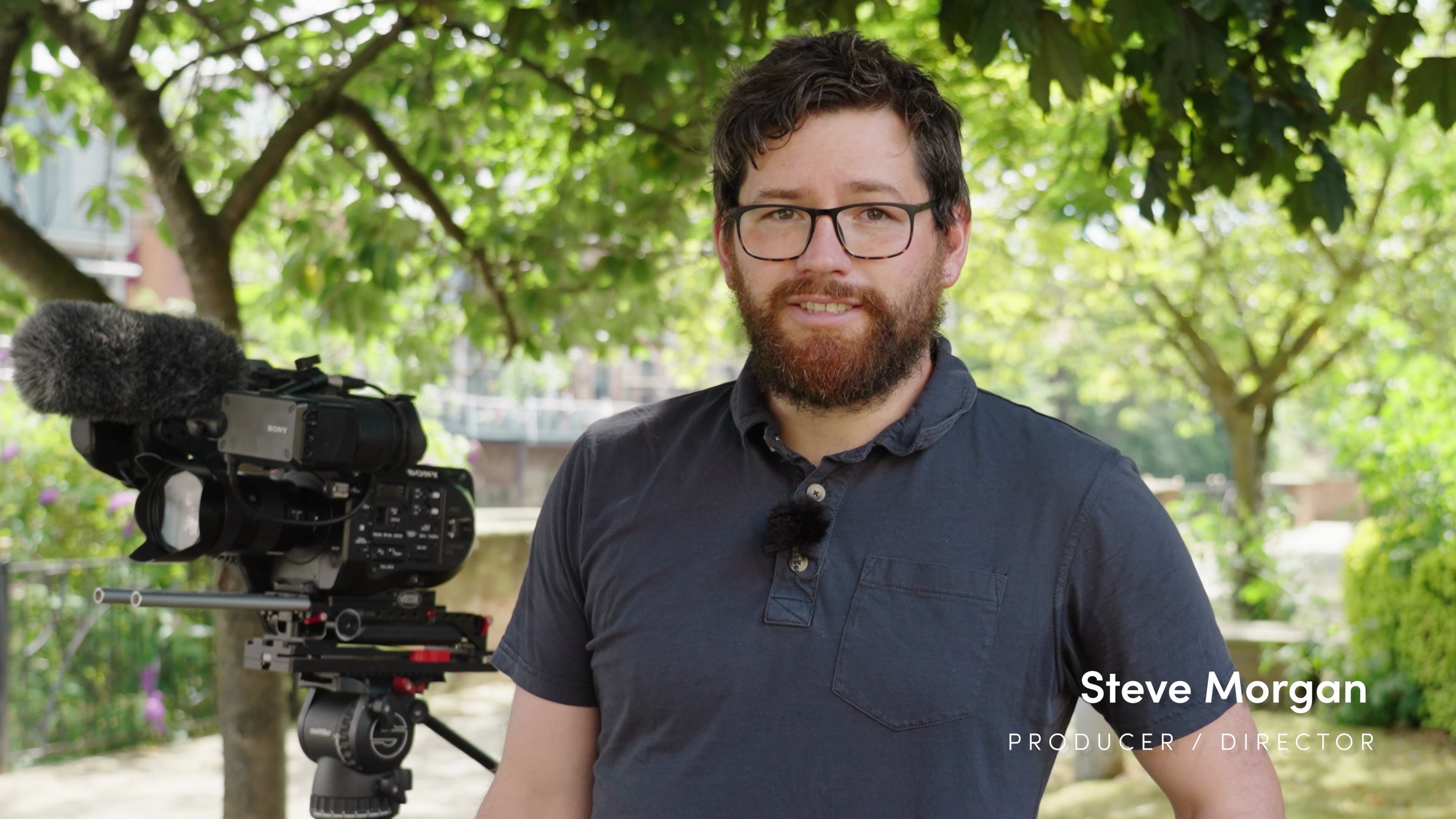 Steve Morgan, producteur-réalisateur de télévision debout à côté d'une Sony FS7 sous un auvent de feuilles d'arbre à York.