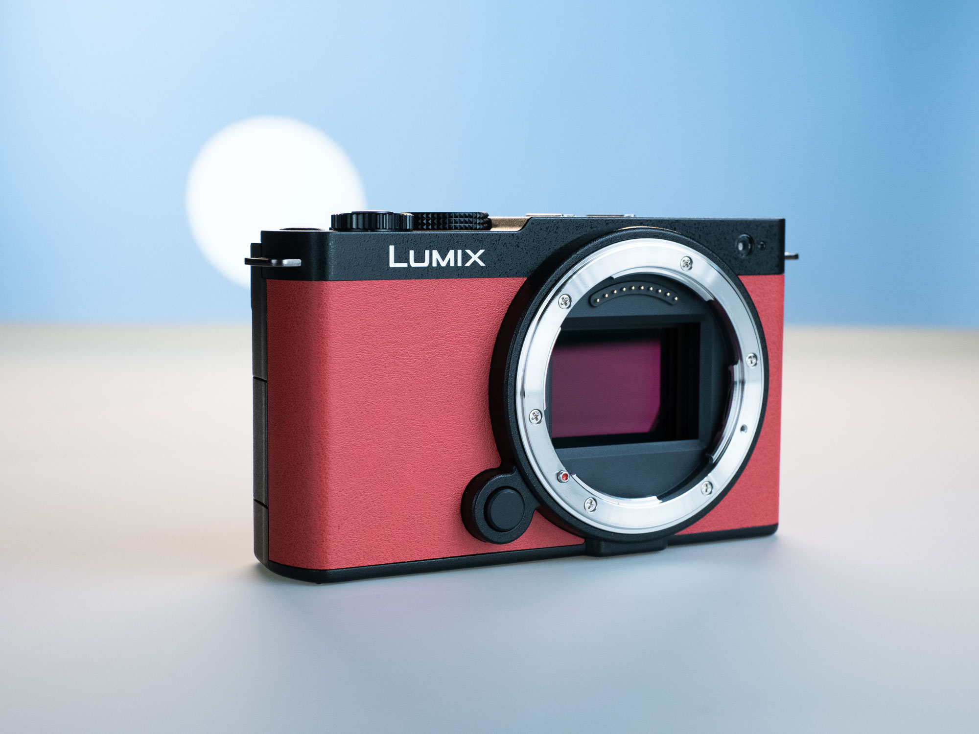 A red Panasonic Lumix S9 body on a light blue and light grey backdrop. A soft white circle is in the background.