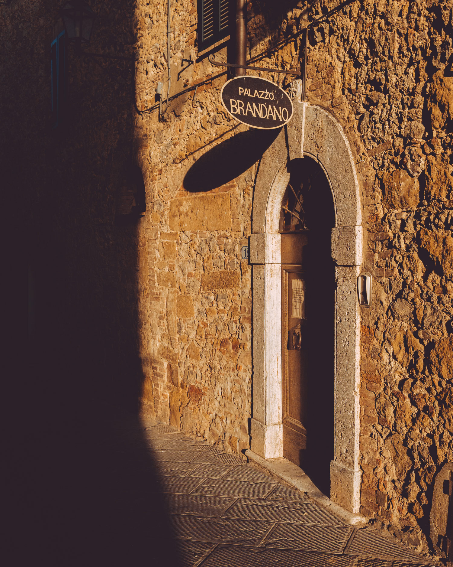 A door on a street in sunlight in Petrolo, Tuscany. Palazzo Brandano is written on a sign above the door.