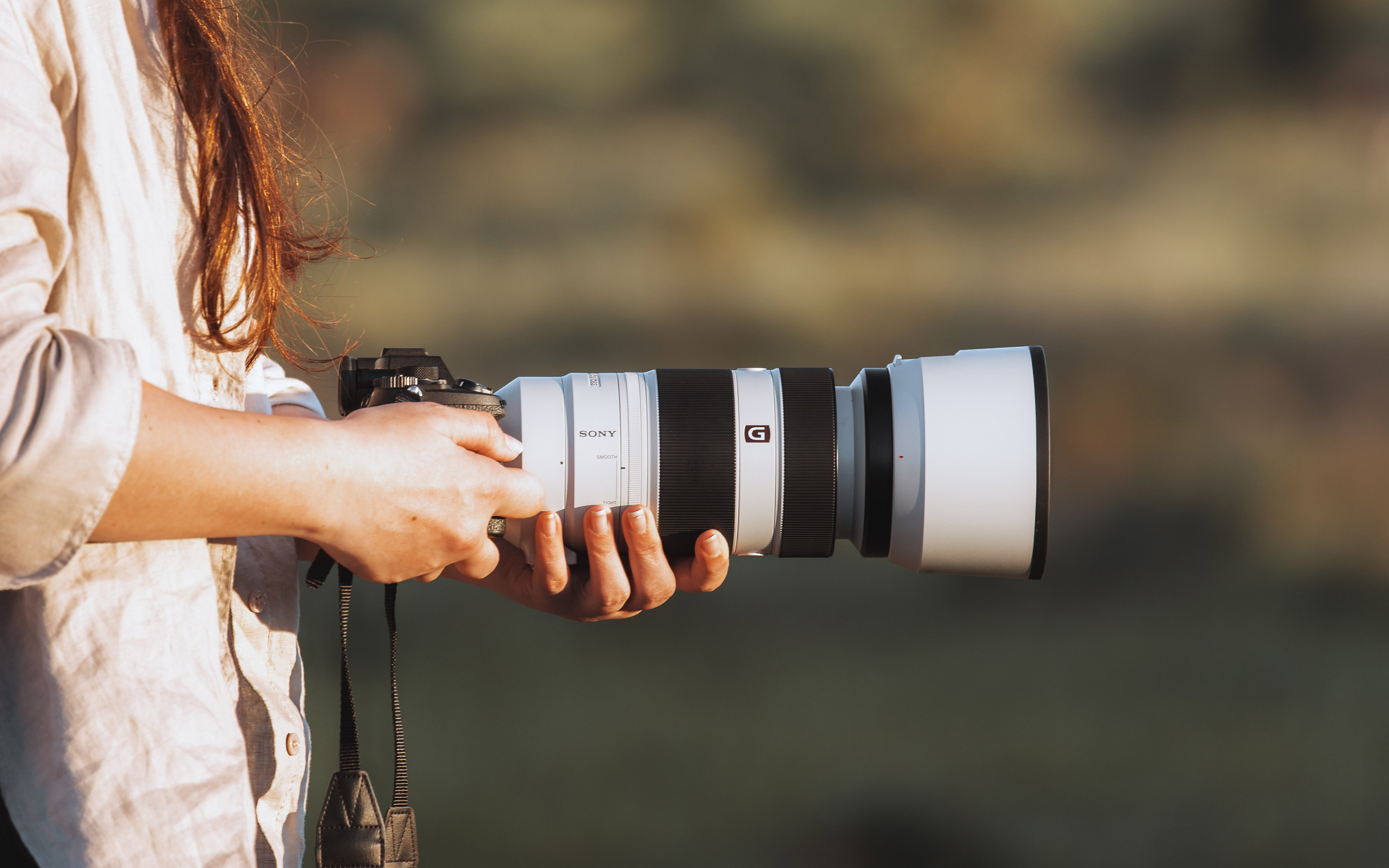 Sony A7 IV en Sony FE 100-400mm f/4.5-5.6 GM OSS lens vanaf de zijkant, vastgehouden door een persoon in beide handen
