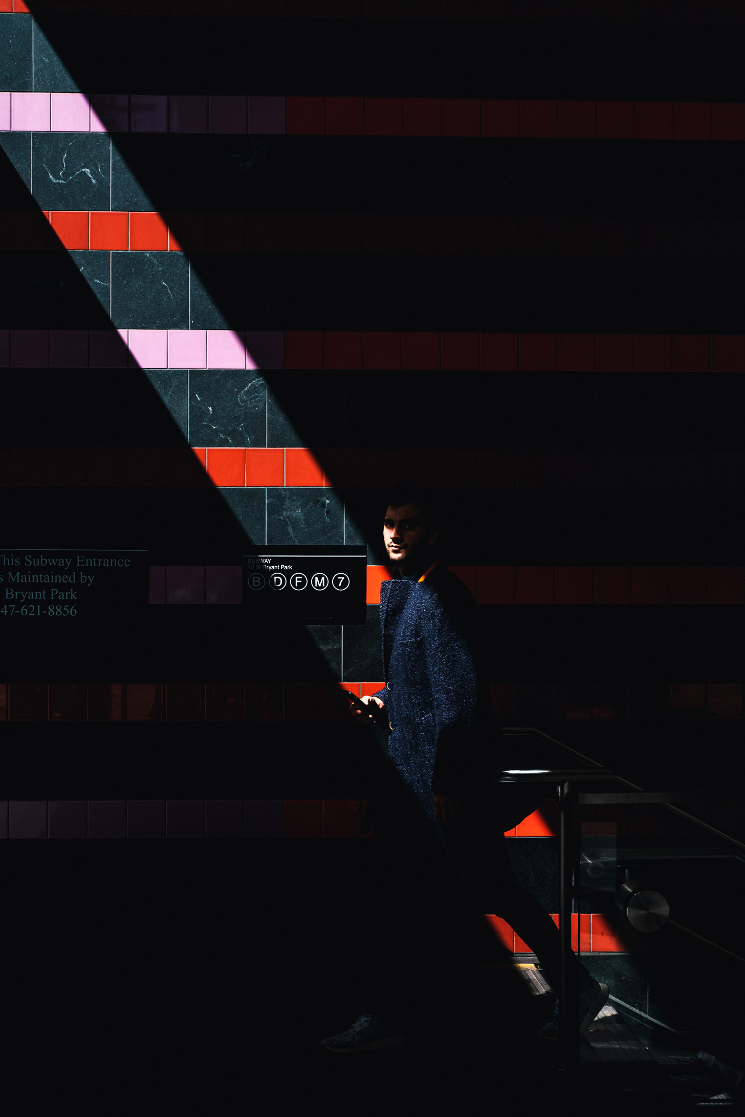 Persoon loopt uit de NYC metro met rood gestreepte muur in de zon.