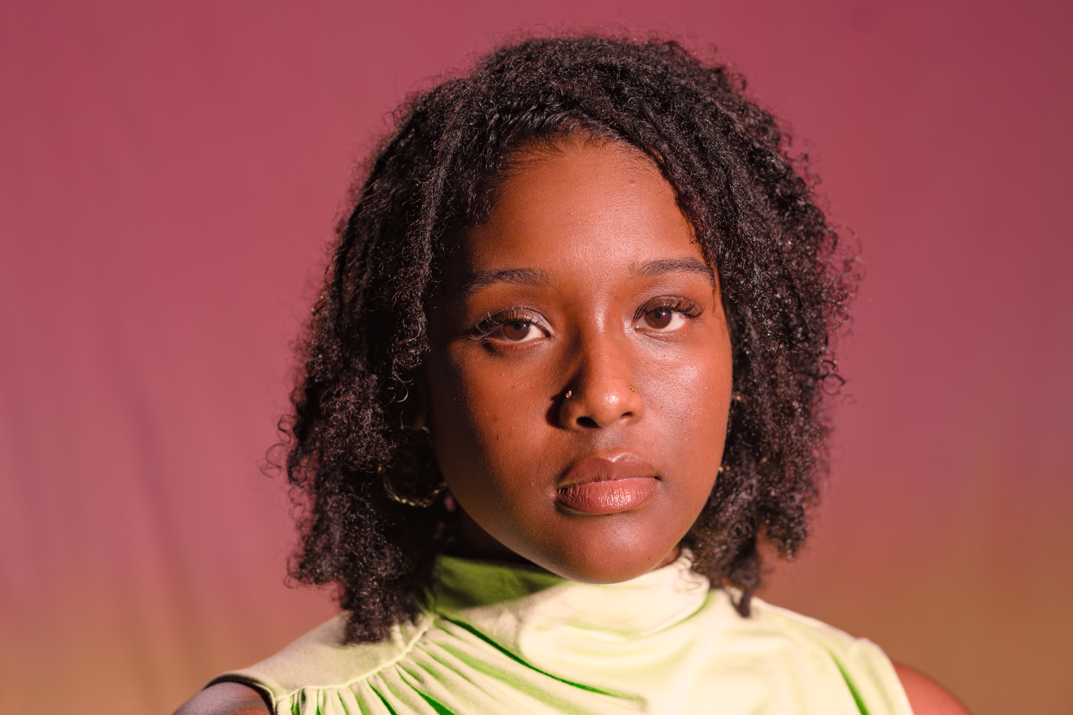 Person with black curly hair and a green top looking directly at the camera. Photographed by Kaylah Sambo on a Hasselblad X1D-50c.