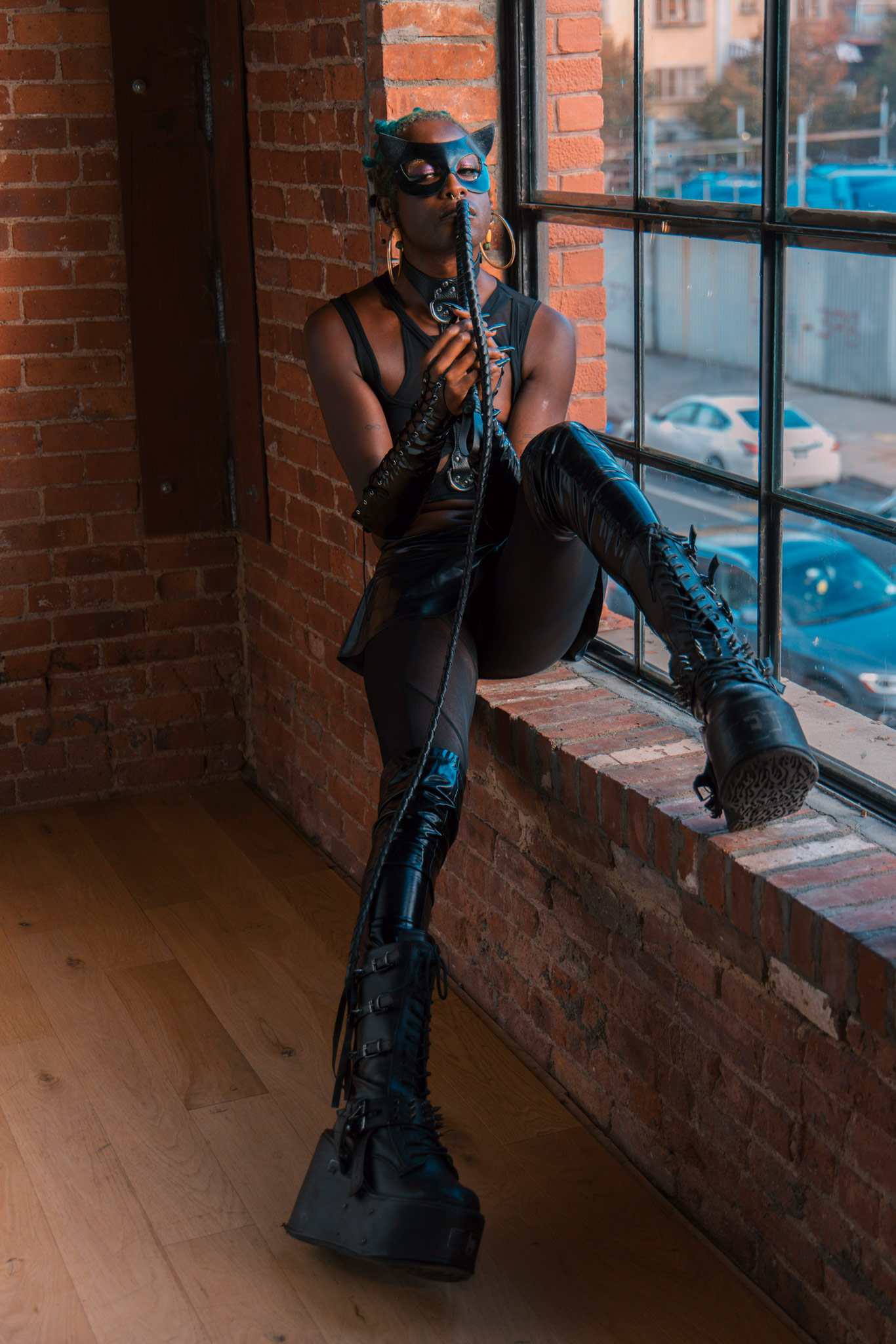 Catwoman cosplayer sits against a window.

