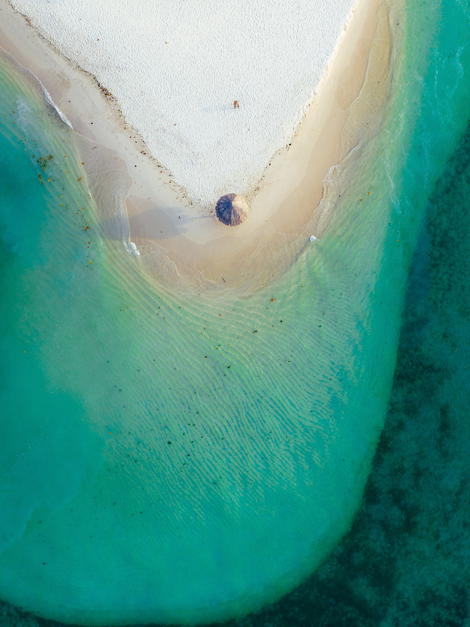 Drone aerial photo of a white sand shoreline and clear turquoise sea, showing shallow water patterns near the beach.