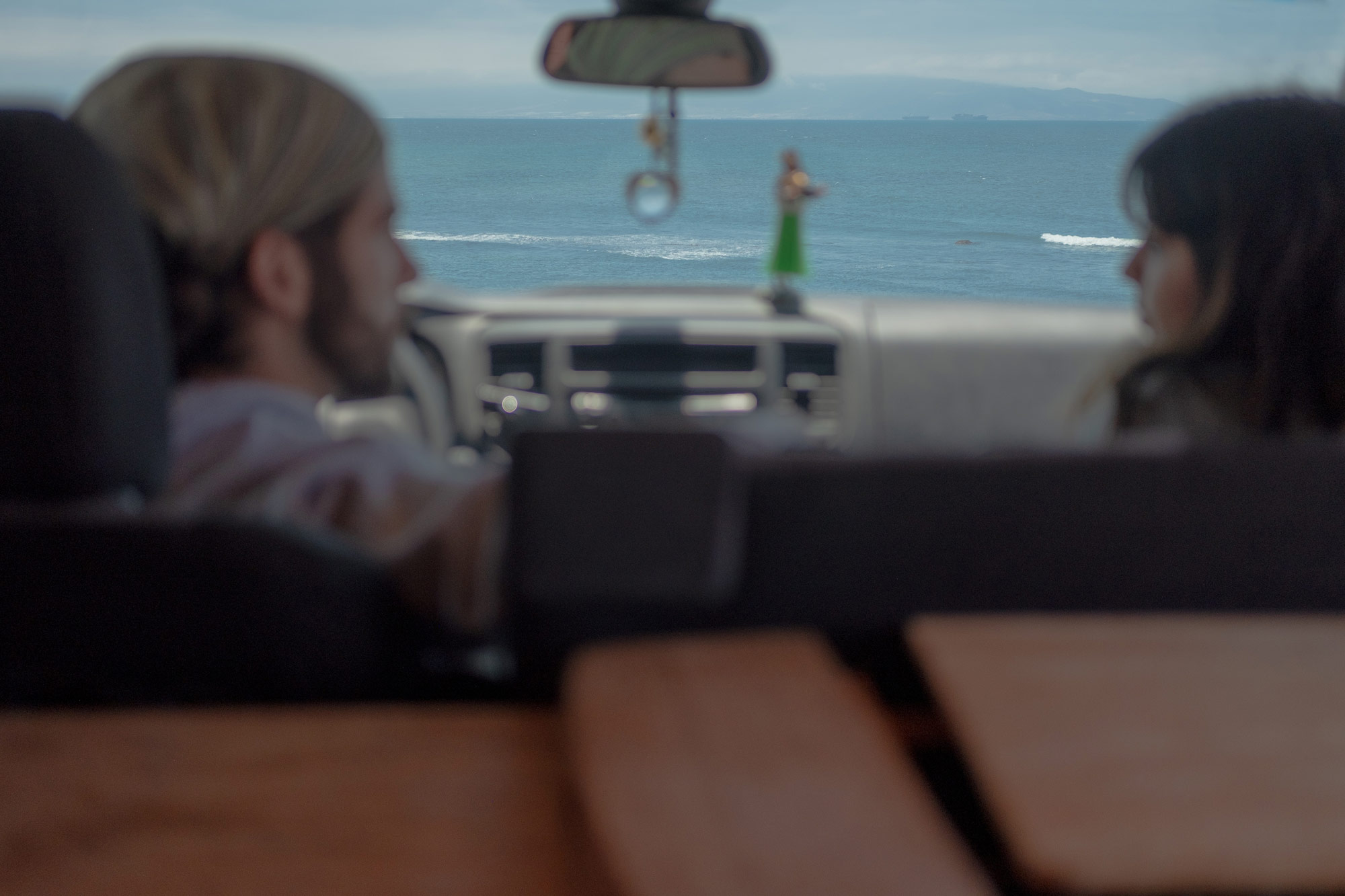 Two people looking at each other in a vehicle in front of a body of water.