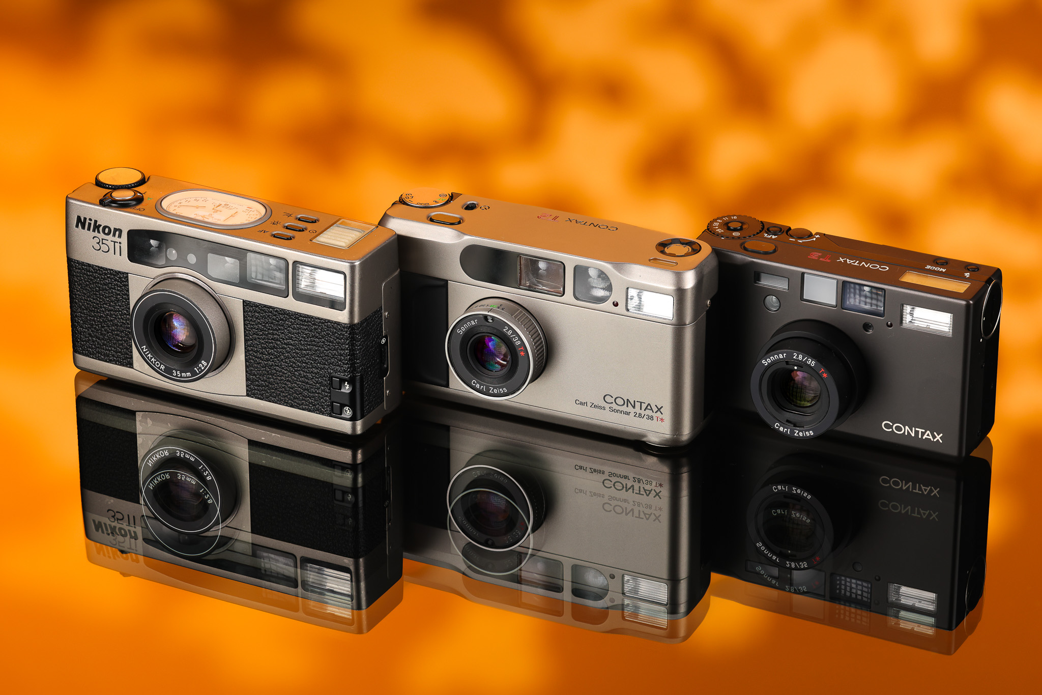 A collection of the Contax T2, Contax T3 and Nikon 35Ti on an orange and brown background.