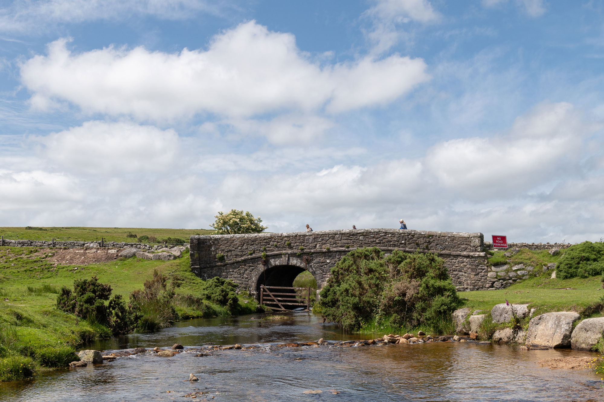 A long dry stone wall stretches out across the landscape, with a road in front of it. Blue sky with white clouds can be seen above. Photo by Amy Moore with the Panasonic S1R II.