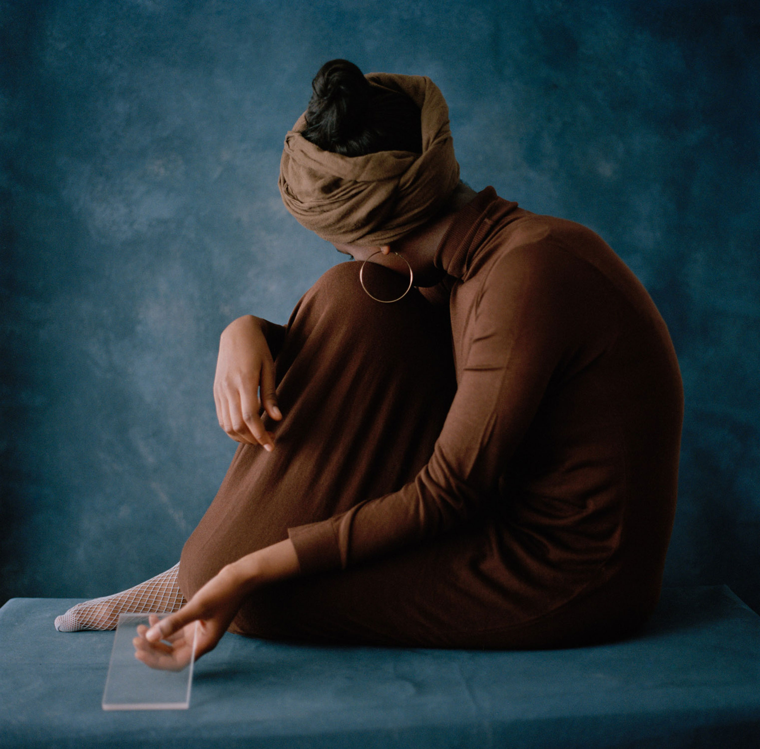 Black woman sitting with one leg bent and turning her head away from the camera, hiding her face behind the bent leg, shot by Nicole Benewaah 


