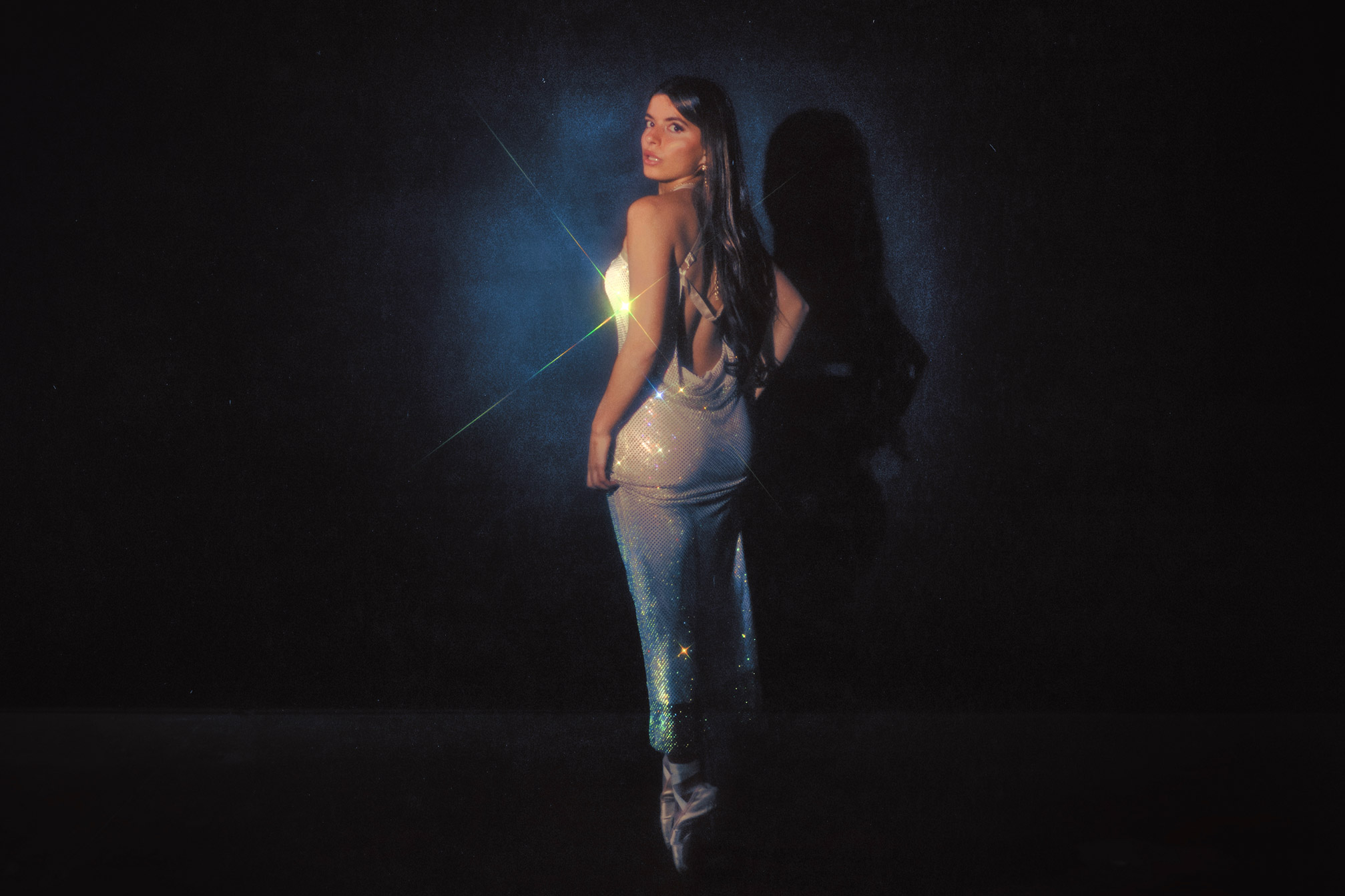 Person in sparkly white dress looking back in front of a blue backdrop, photo by Brandon Woelfel