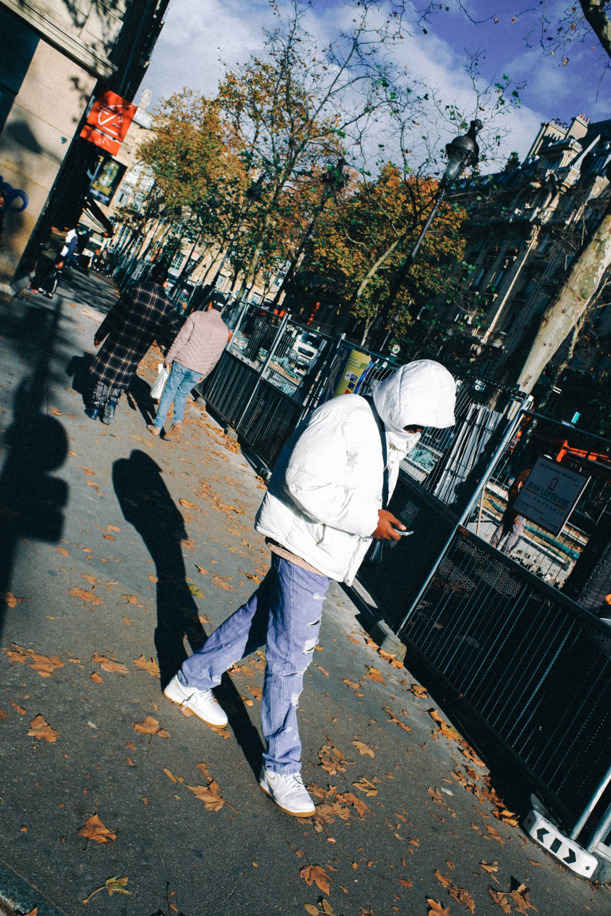 A candid Paris street scene in autumn, featuring pedestrians, long shadows and crisp sunlight against colourful fall leaves and classic city architecture. Shot by Wesley Verhoeve on a Fujifilm XF10.