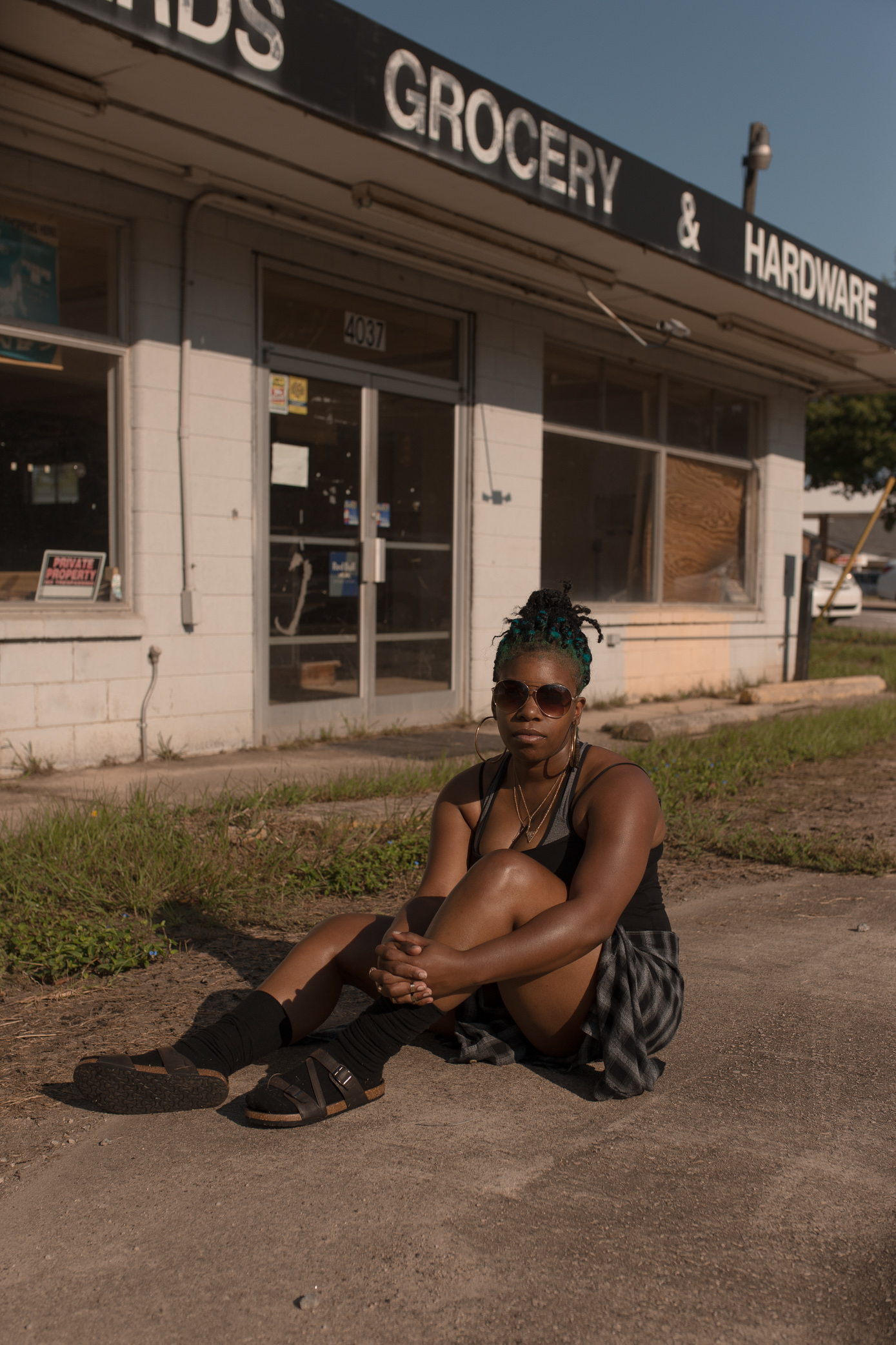 Photo of black woman in front of abandoned convenience store sitting on the ground