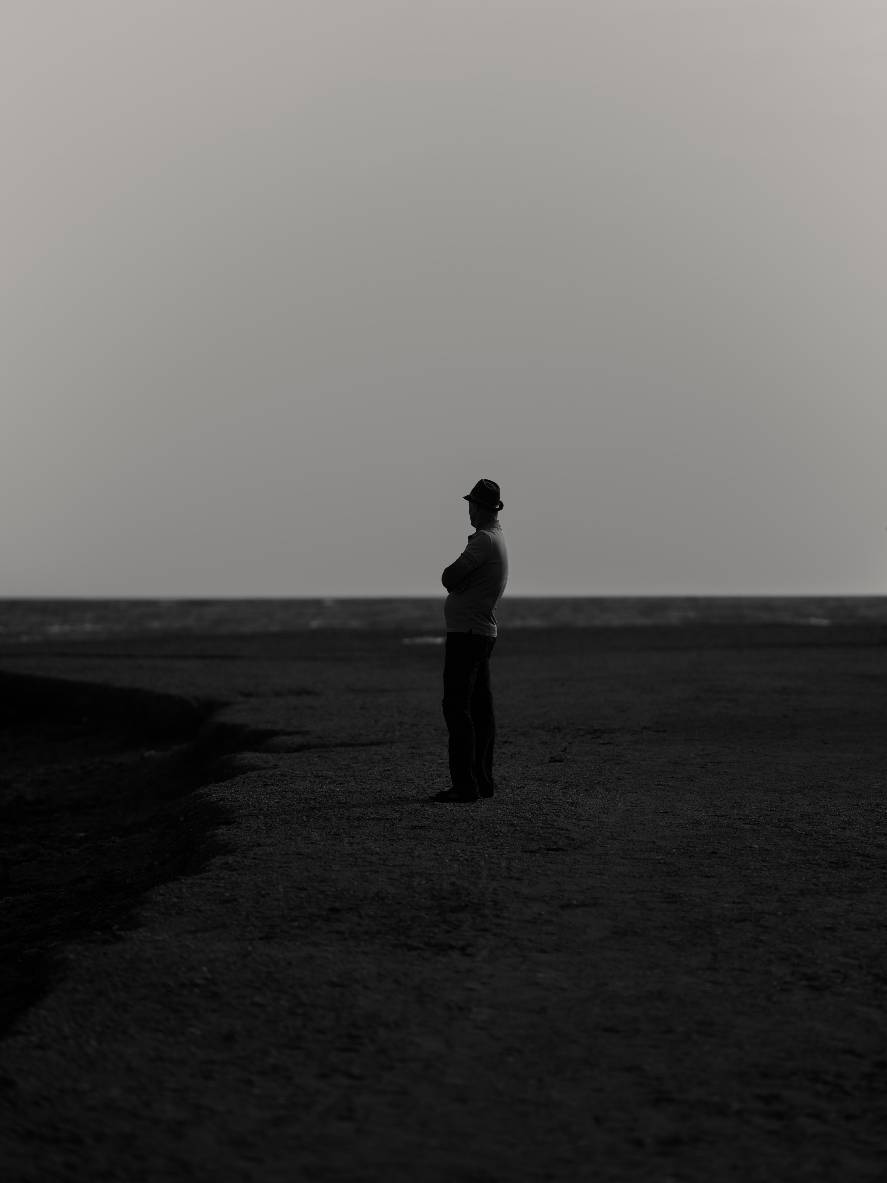 Black and white photo of a person in a hat on a beach staring off in the distance.