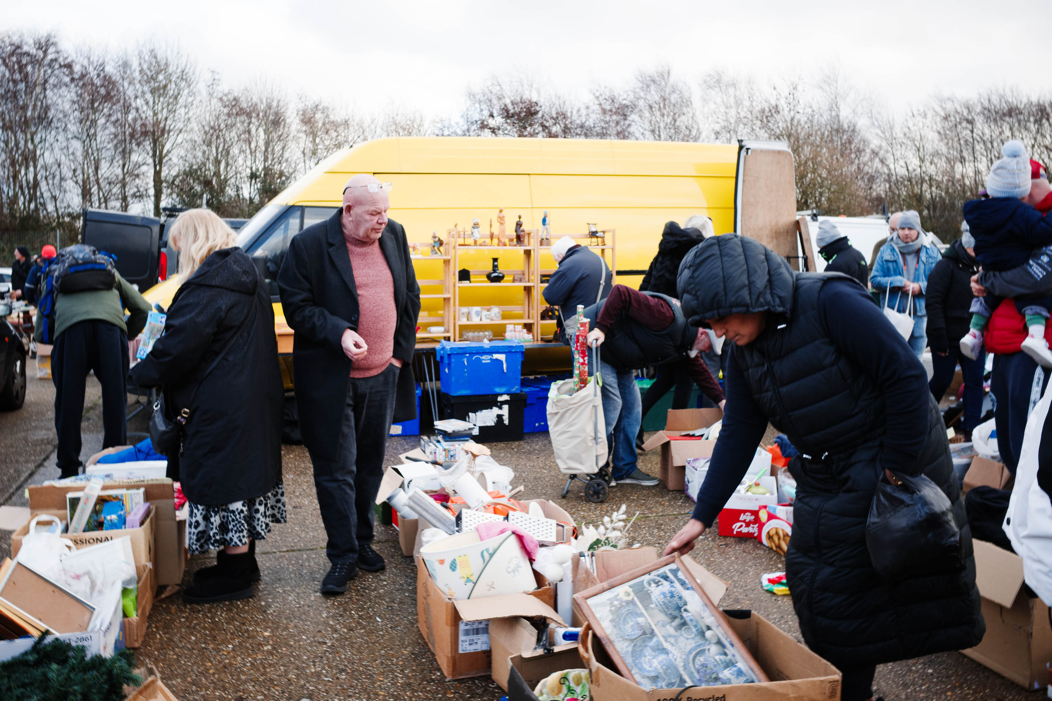 Spontane Szene auf einem Straßenmarkt, die Kisten mit Haushaltsartikeln und Sammlerstücken neben einem leuchtend gelben Van bei natürlichem Tageslicht zeigt. Aufgenommen mit einer Ricoh GR IV.