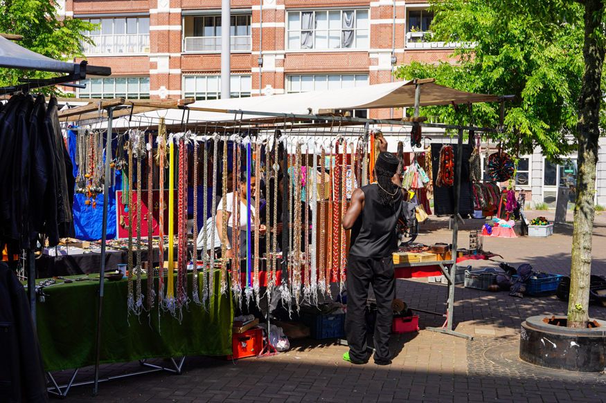 Een kleurrijke sieradenkraam op de Amsterdamse Waterloopleinmarkt, vol kettingen, accessoires en levendige ontmoetingen in helder middaglicht, gefotografeerd door Louise Kluit