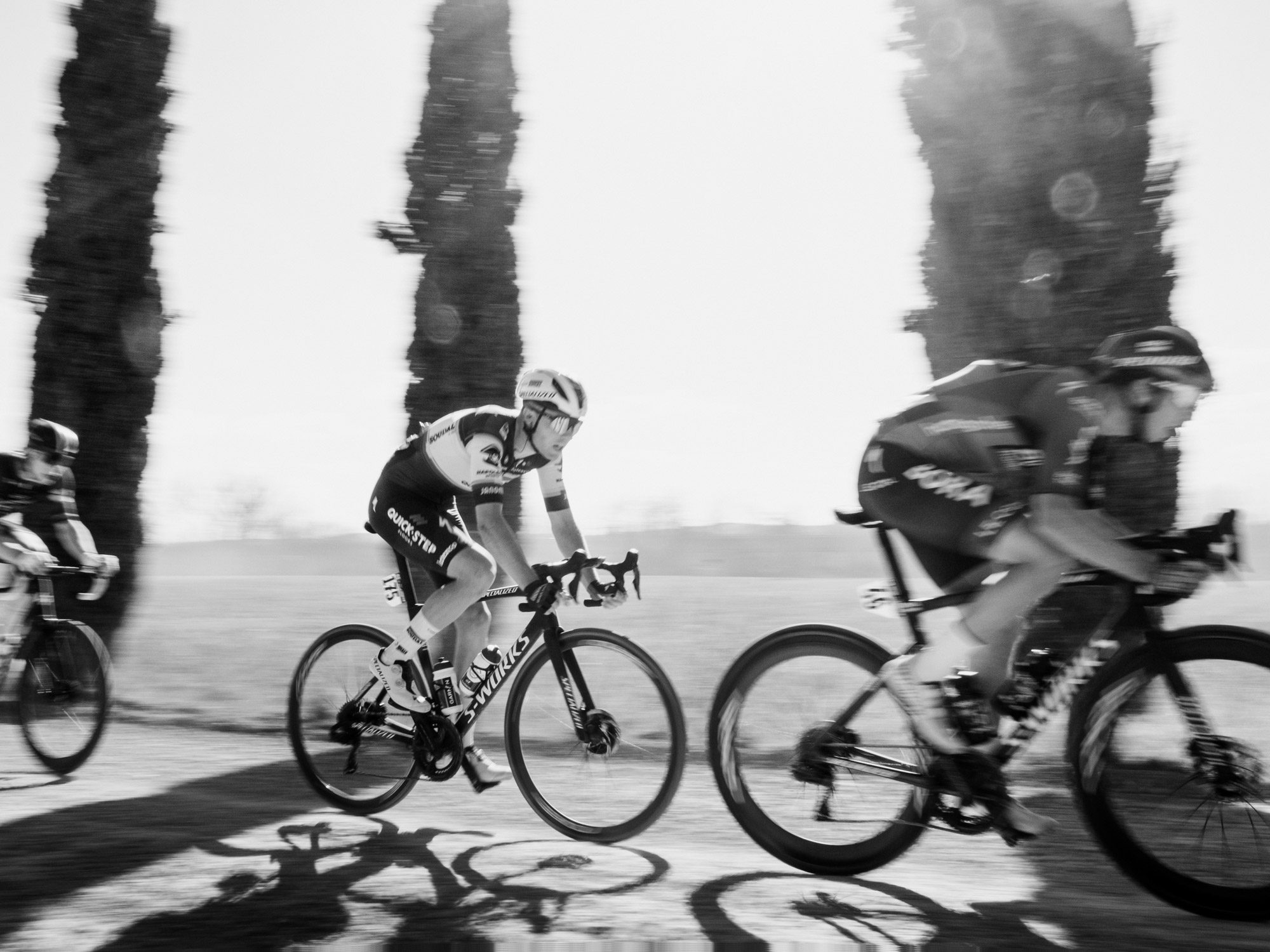 Trois coureurs de l’équipe Jumbo Visma passent à vive allure devant des palmiers dans une image en noir et blanc qui met en valeur le mouvement et le rythme du peloton. Photo : Dan King, réalisée avec un Fujifilm X-Pro 3.