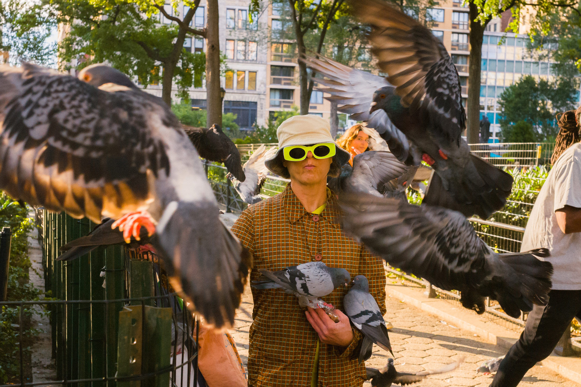 Persoon met een bucket hat en gele zonnebril die duiven vasthoudt in New York City, gefotografeerd door Manuel Pena.